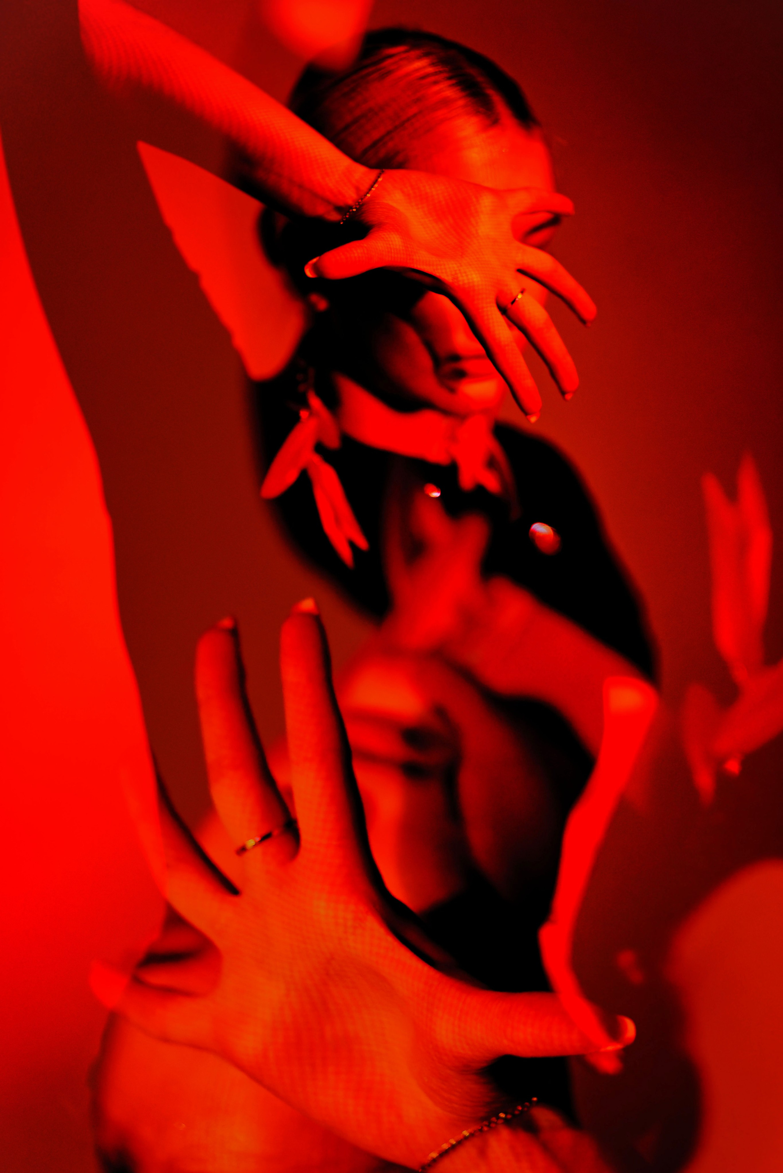 Драматичный портрет с руками закрывающими лицо, интенсивный красный свет, художественная композиция с фокусом на руках