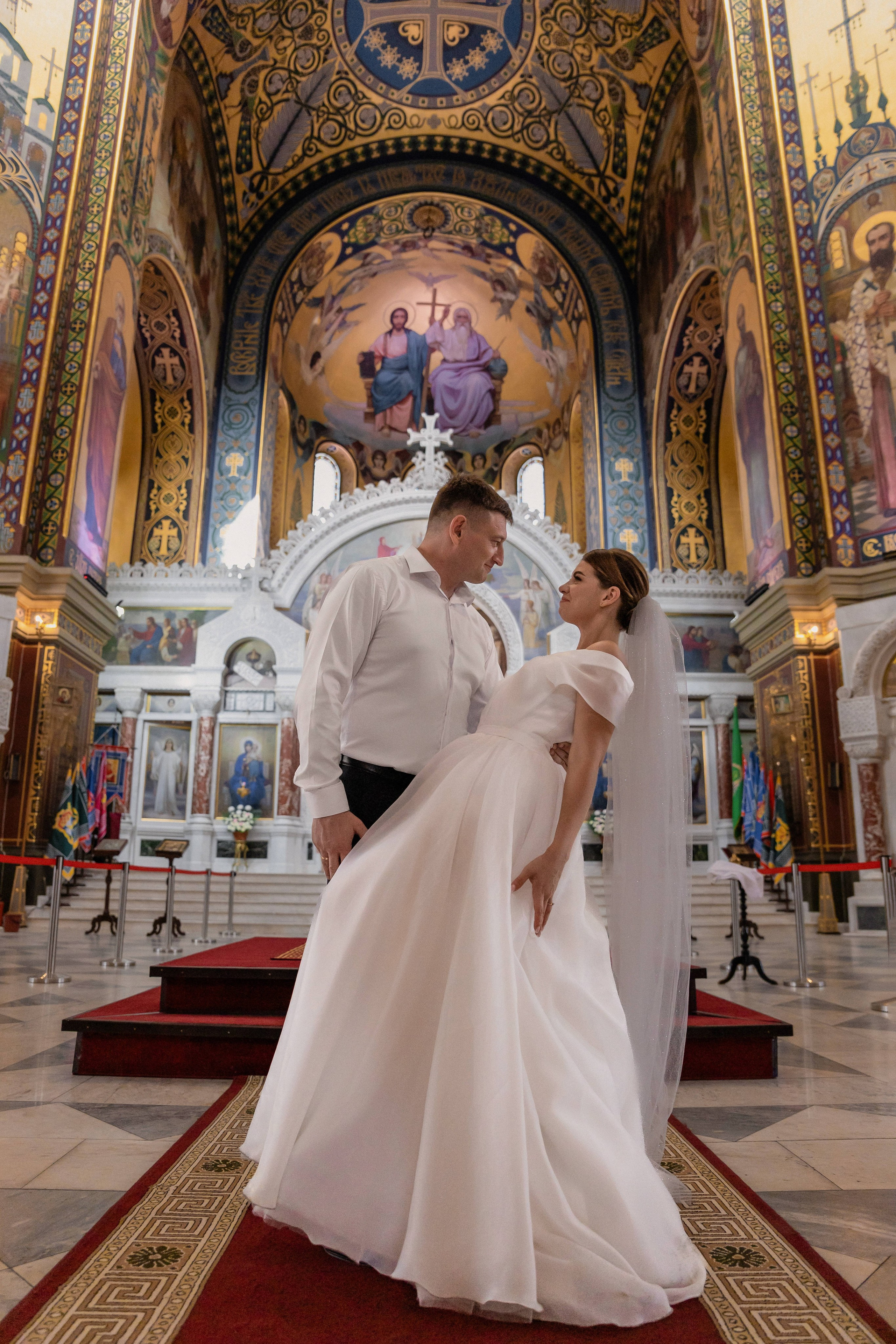 Муж с женой в день венчания стоят и смотрят друг на друга на фоне алтаря в кафедральном Вознесенском соборе в г. Новочеркасск