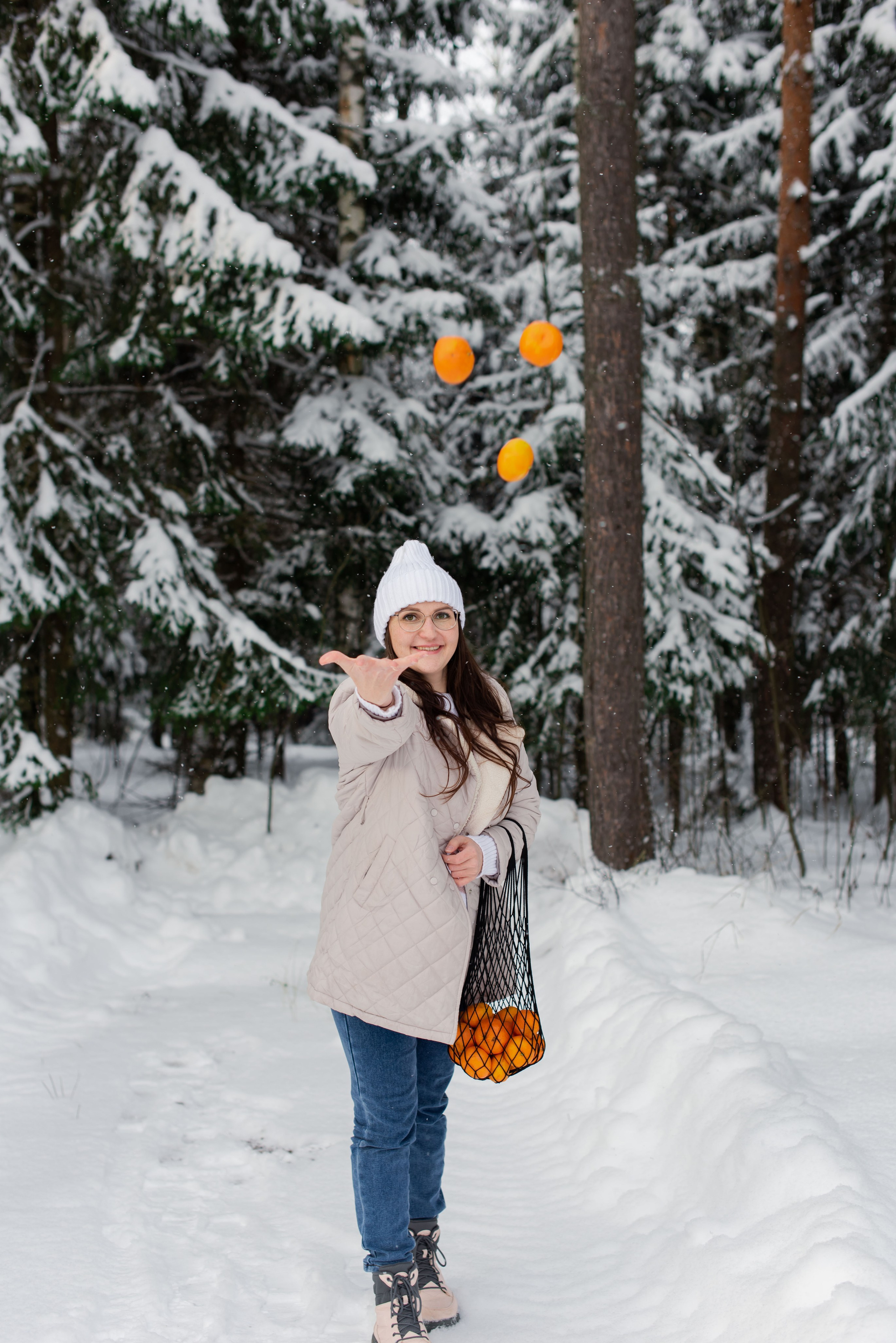 Живой кадр: женщина со смехом подбрасывает мандарины в заснеженном зимнем лесу, Королёв