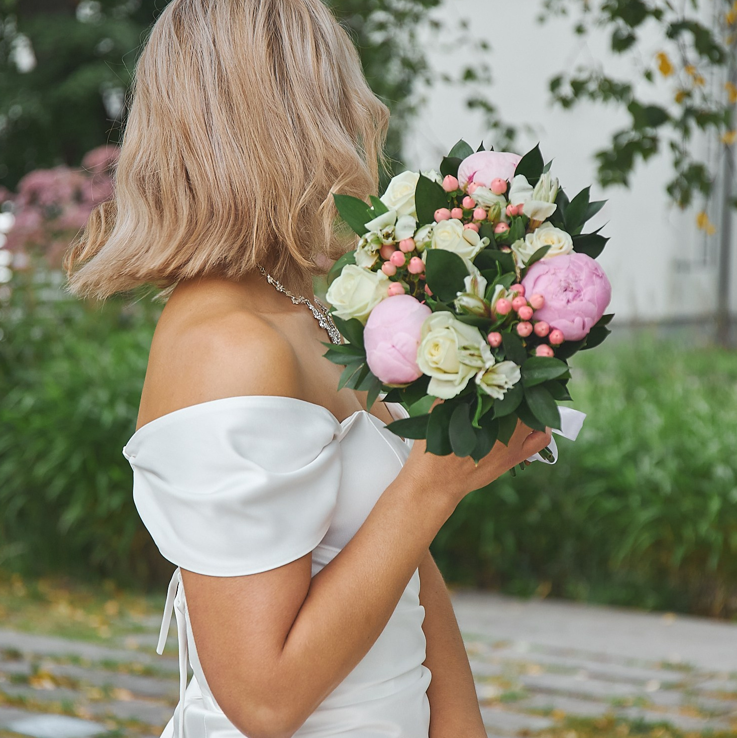 Невеста в белом платье отвернулась от камеры. 