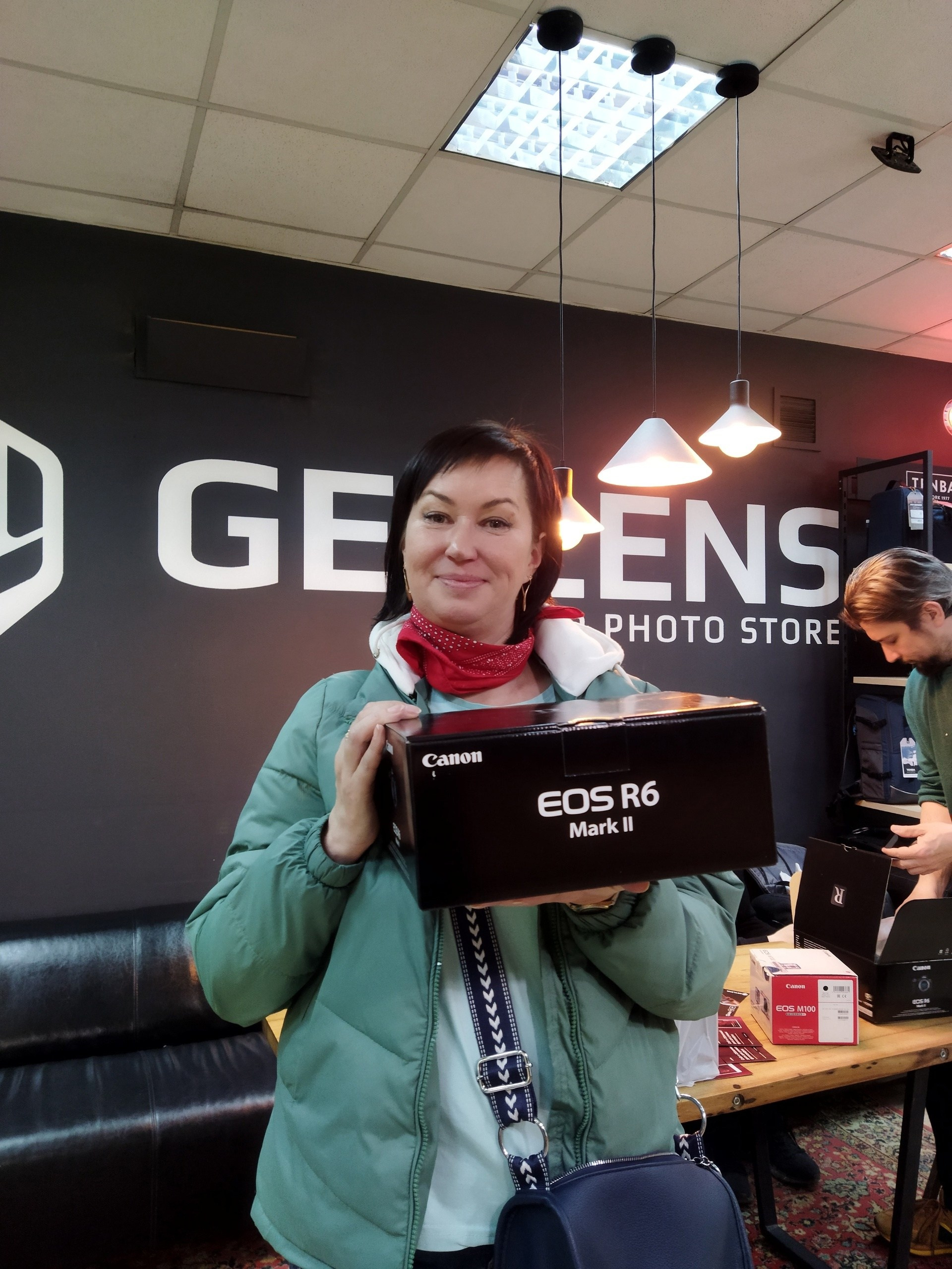 девушка стоит в шоуруме get lens на руках держит коробку от нового фотоаппарата canon r6 m 2