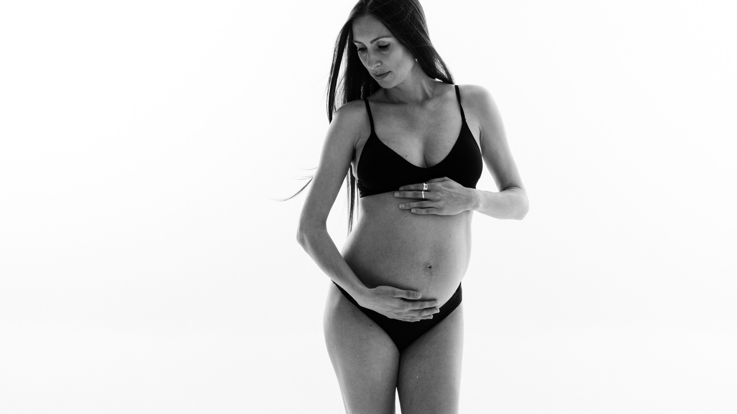 Pregnancy Boudoir photographer London — full body portrait in lingerie on white background, minimalist and empowering style, woman touching Her Belly