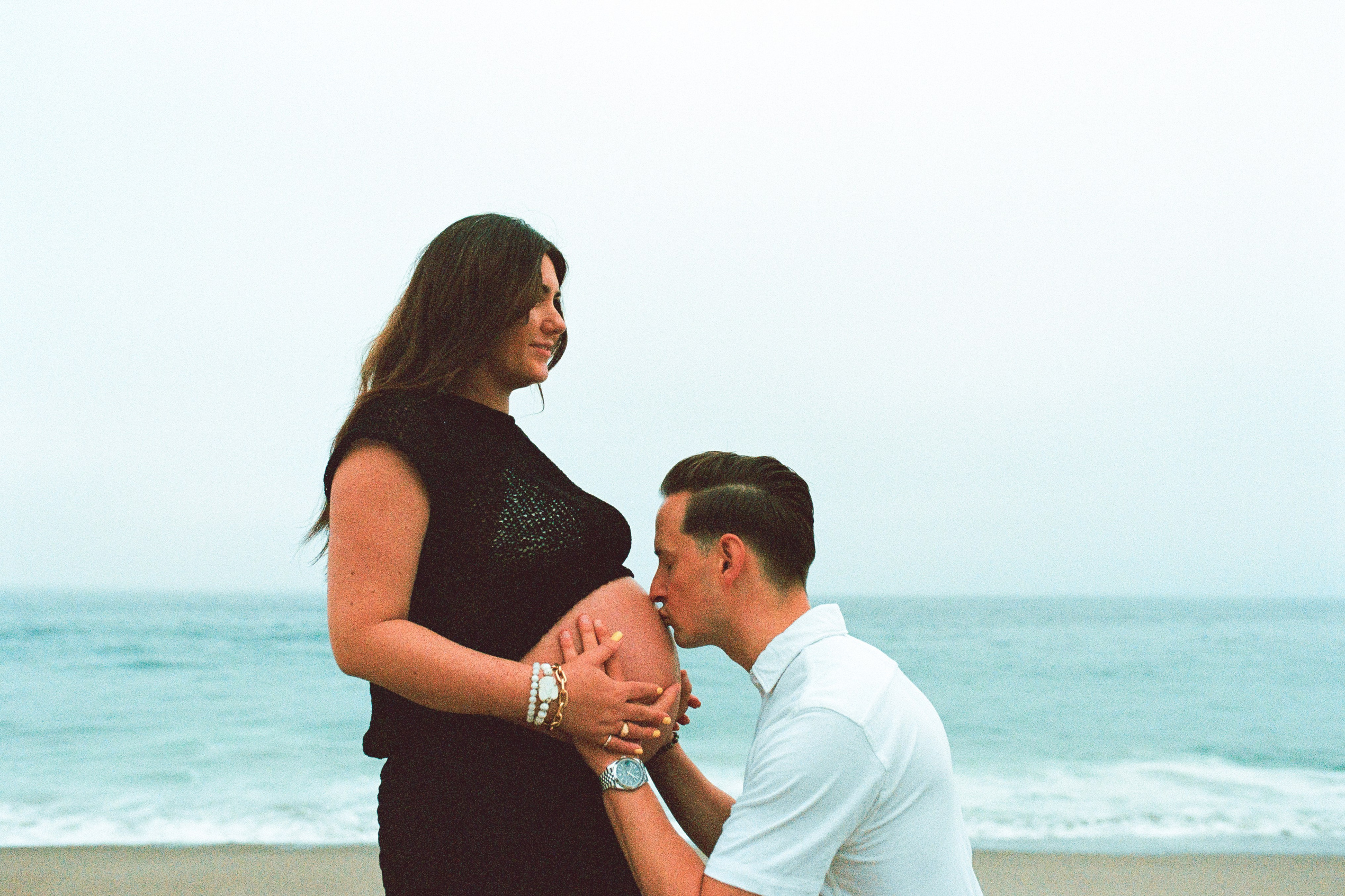 a film photo of a husband kissing his wife's pregnant belly standing on one knee