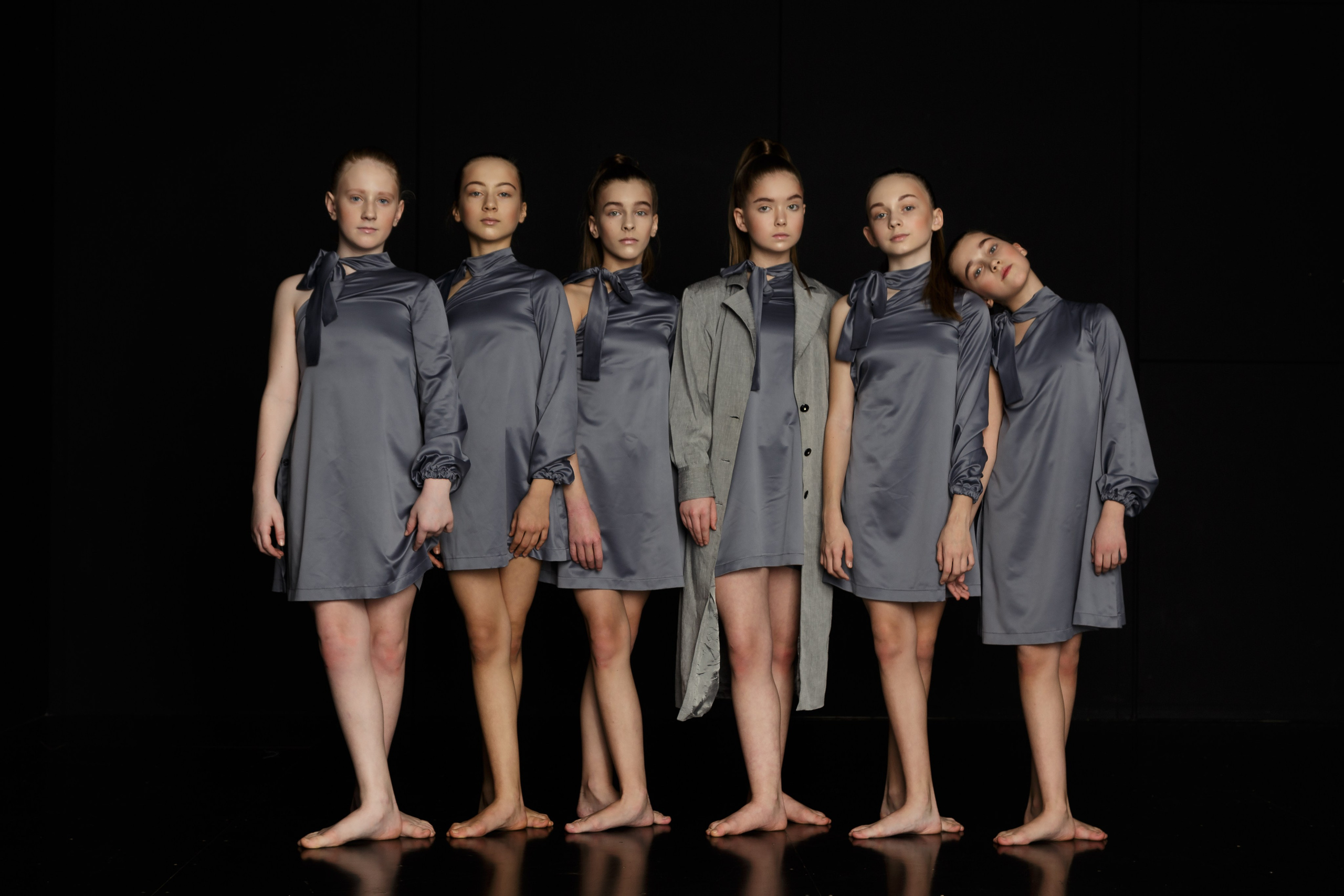 Съемка балета: группа молодых балерин на фоне черного театрального полотна, демонстрирующая грацию и элегантность танца