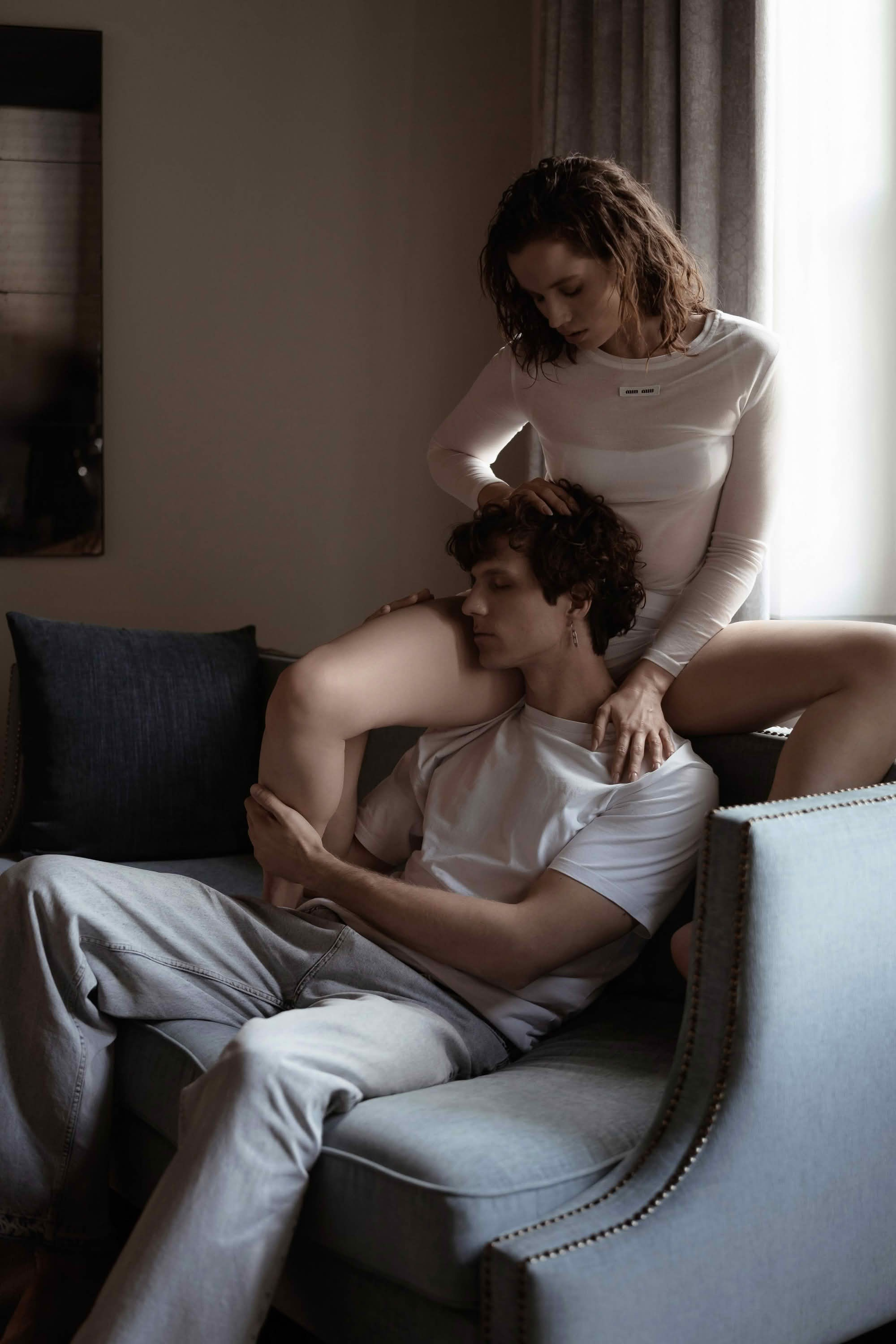 Парная фотосессия СПб — девушка сидит за мужчиной на диване у окна, утренний мягкий свет, домашняя атмосфера