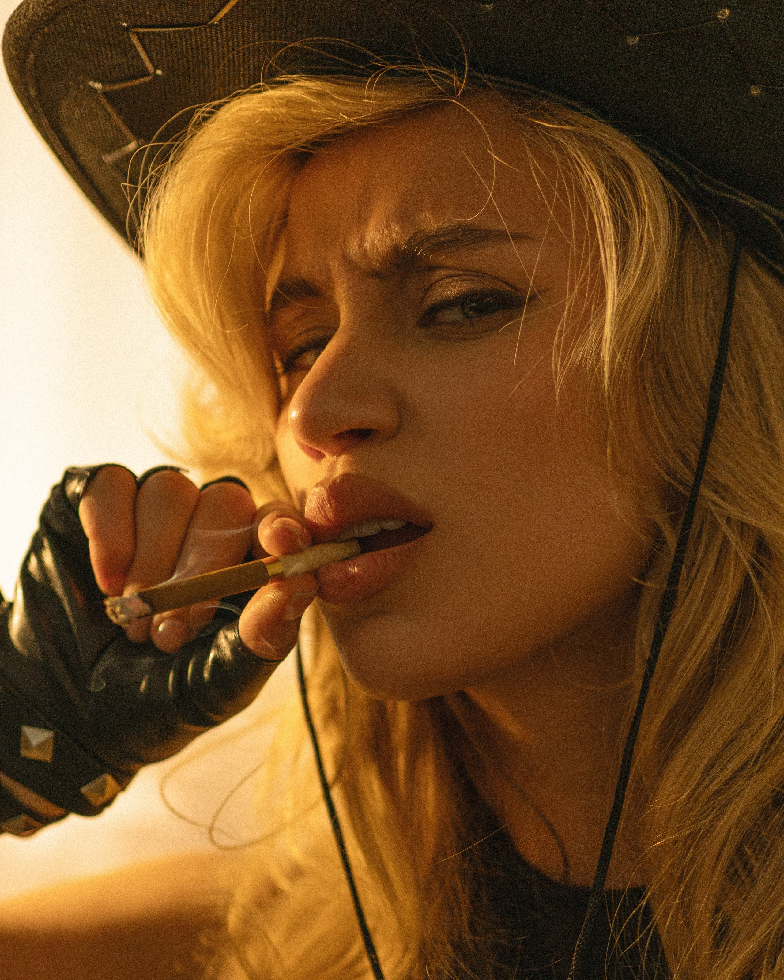 Девушка с сигарой во рту в ковбойском образе с ухмылкой 