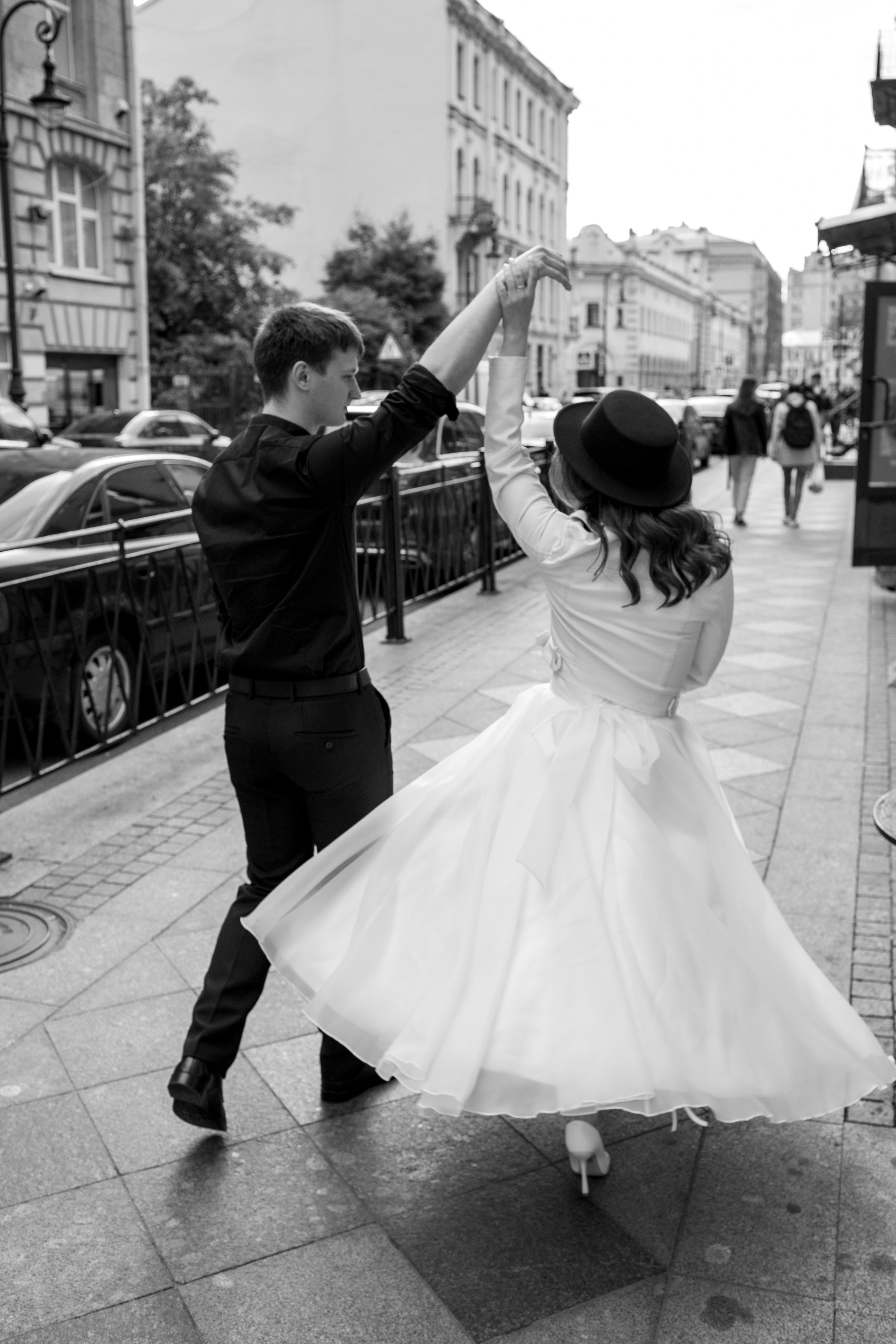 Черно-белая фотография в движении: жених кружит невесту на улице Петербурга.