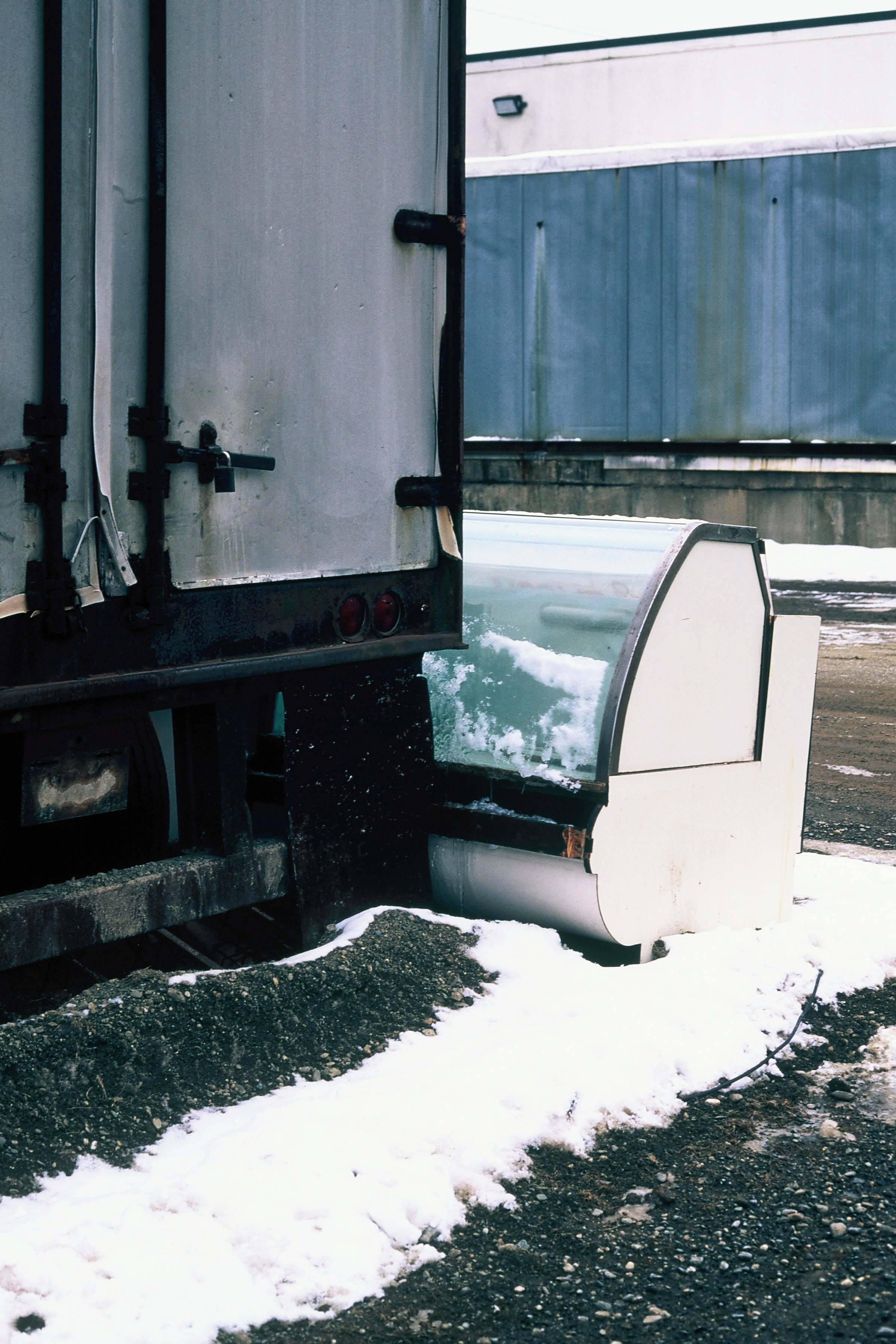 Прицеп грузовика стоит в сугробе, уперевшись в старый морозильник для магазина. США