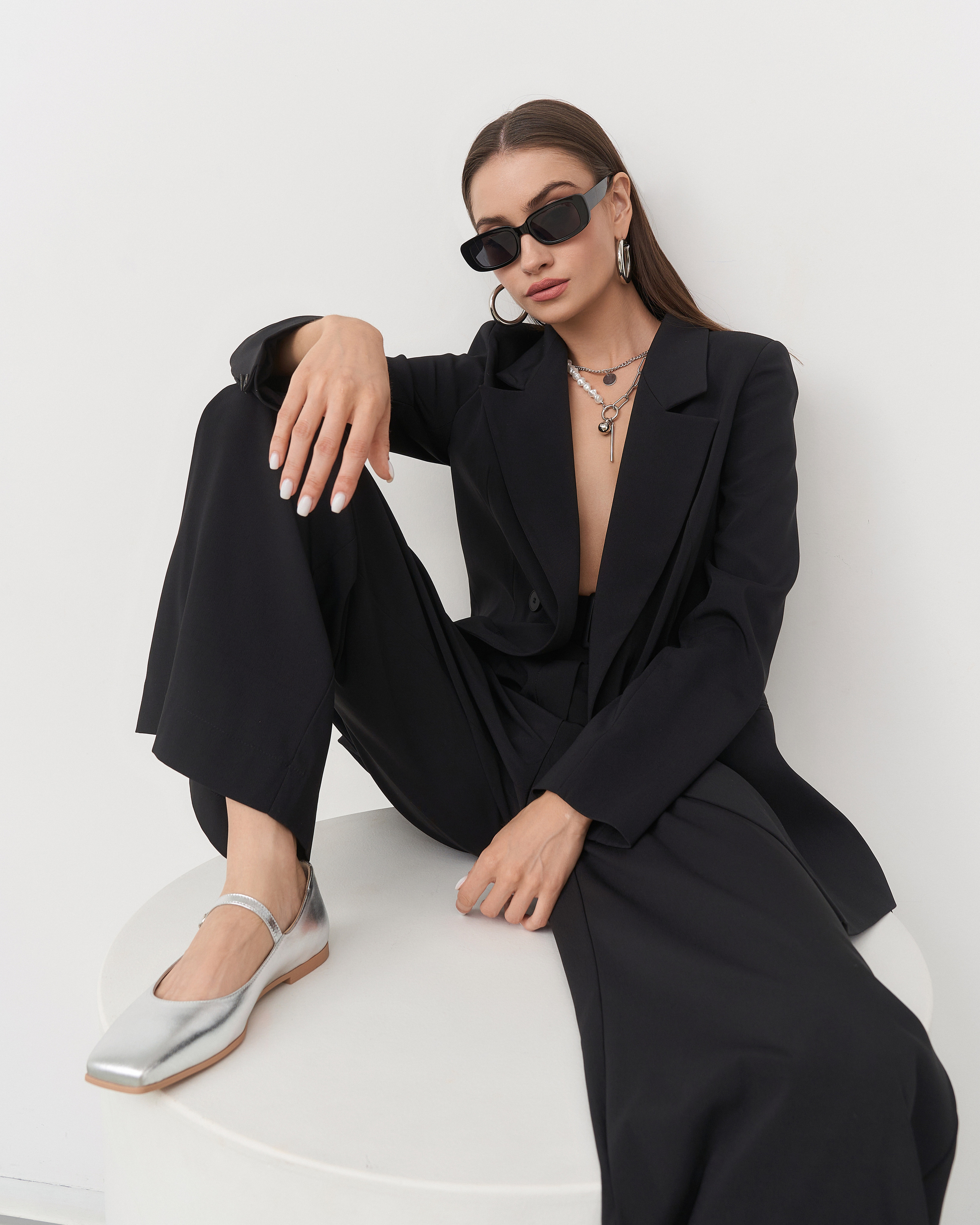 Черный костюм Brandwomen — модель сидит, демонстрируя посадку по фигуре. Циклорама, профессиональный свет