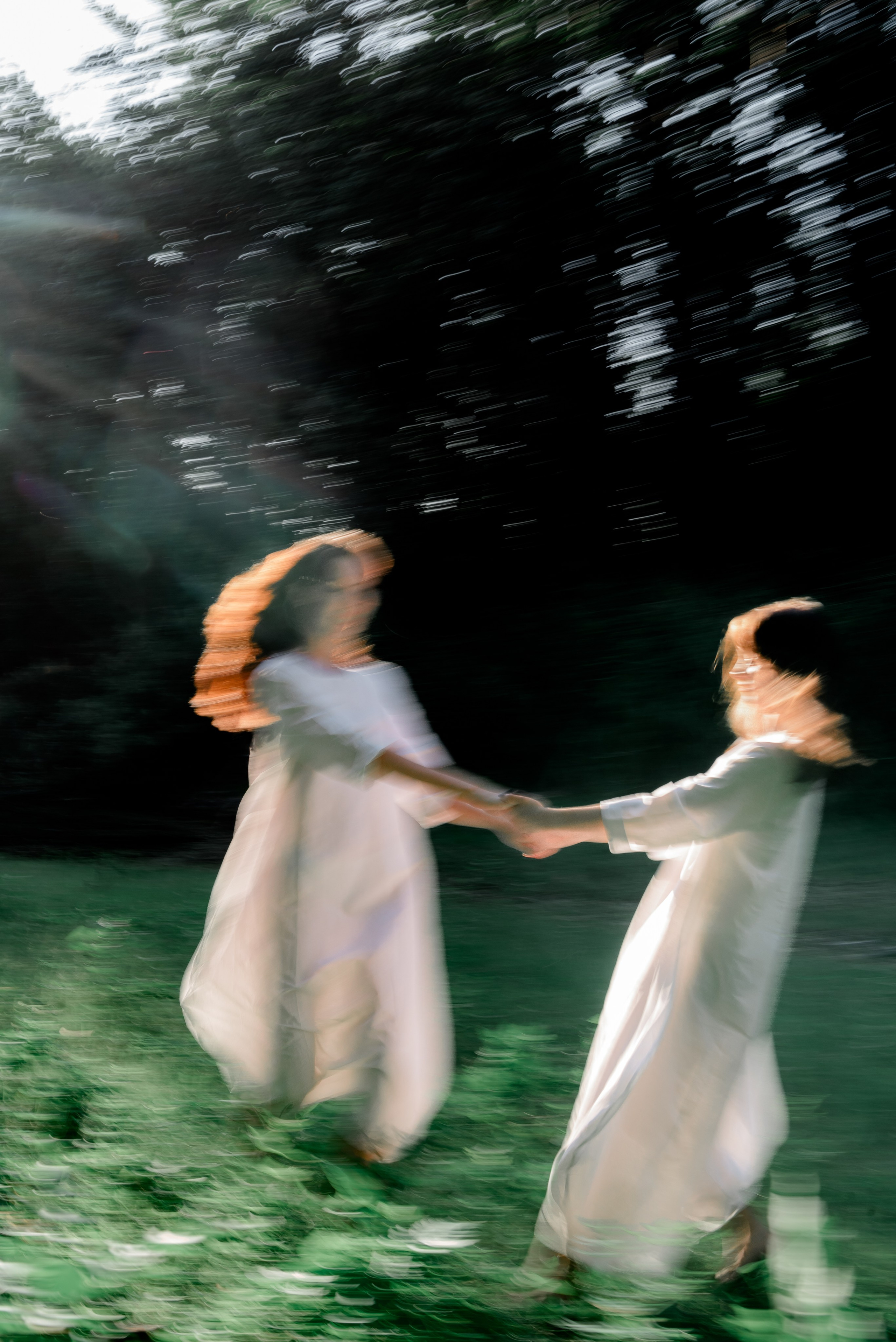 Две девушки в Белых платьях в закатных лучах солнца на фоне зелени в траве бегают и кружится друг вокруг друга