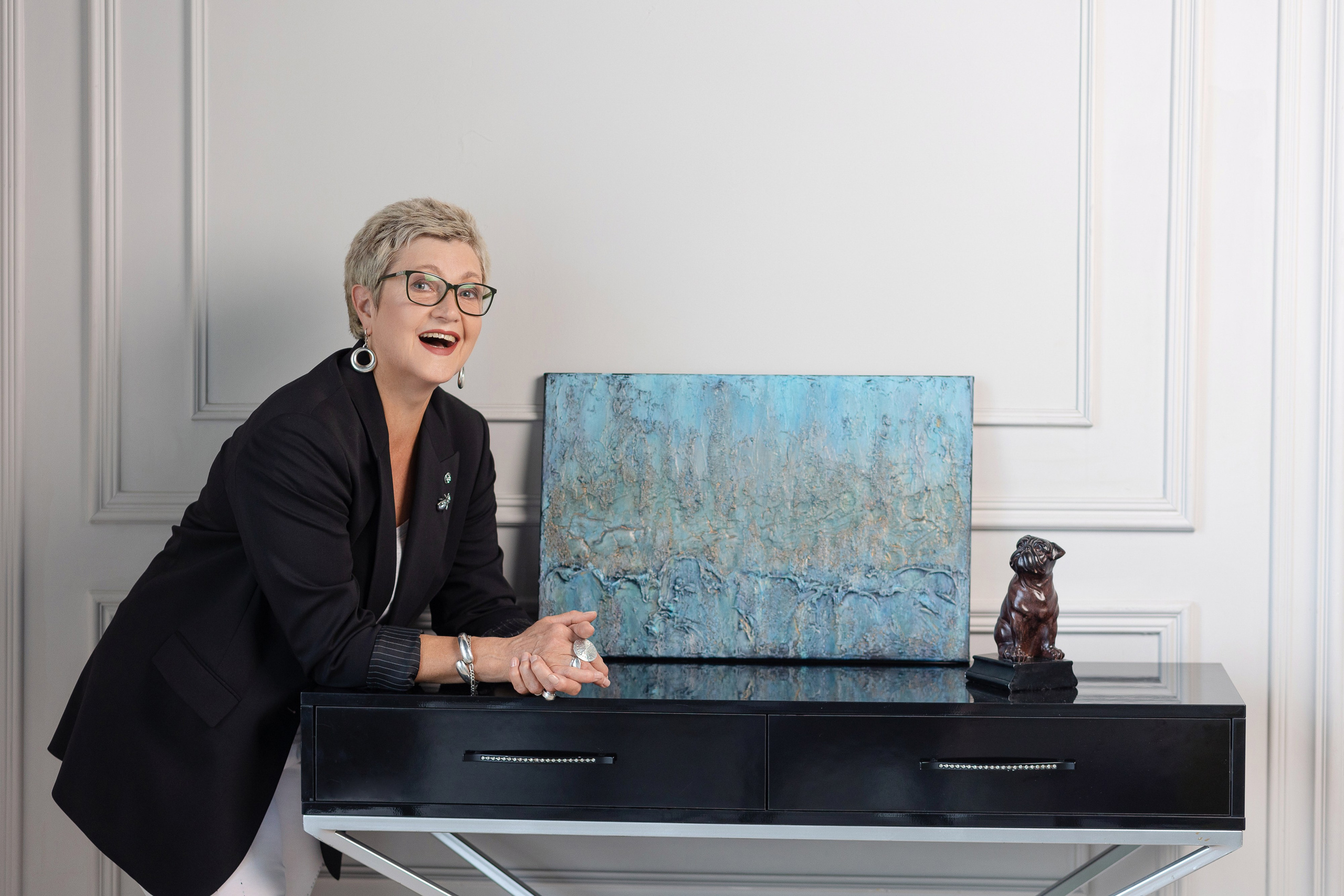 Художница сидит у стола, на котором стоит написанная ею картина.