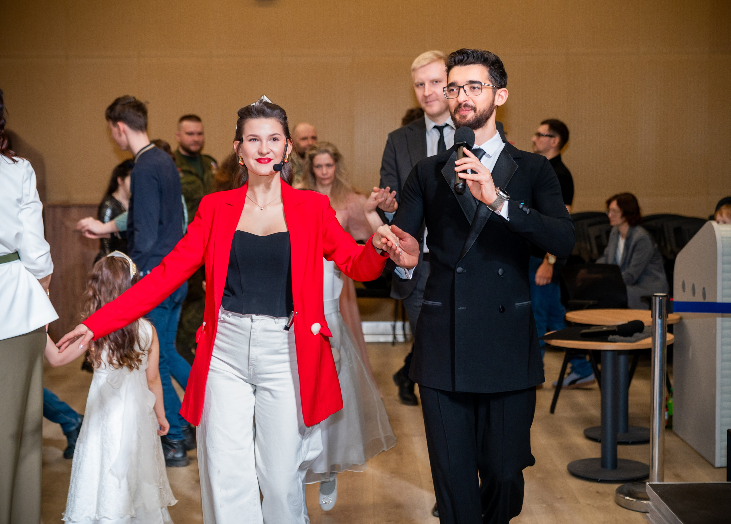Ведущий в чёрном смокинге с микрофоном и женщина в ярко-красном жакете открывают инклюзивный бал проекта «Мы все равны». Фотограф Мальцев Евгений.
