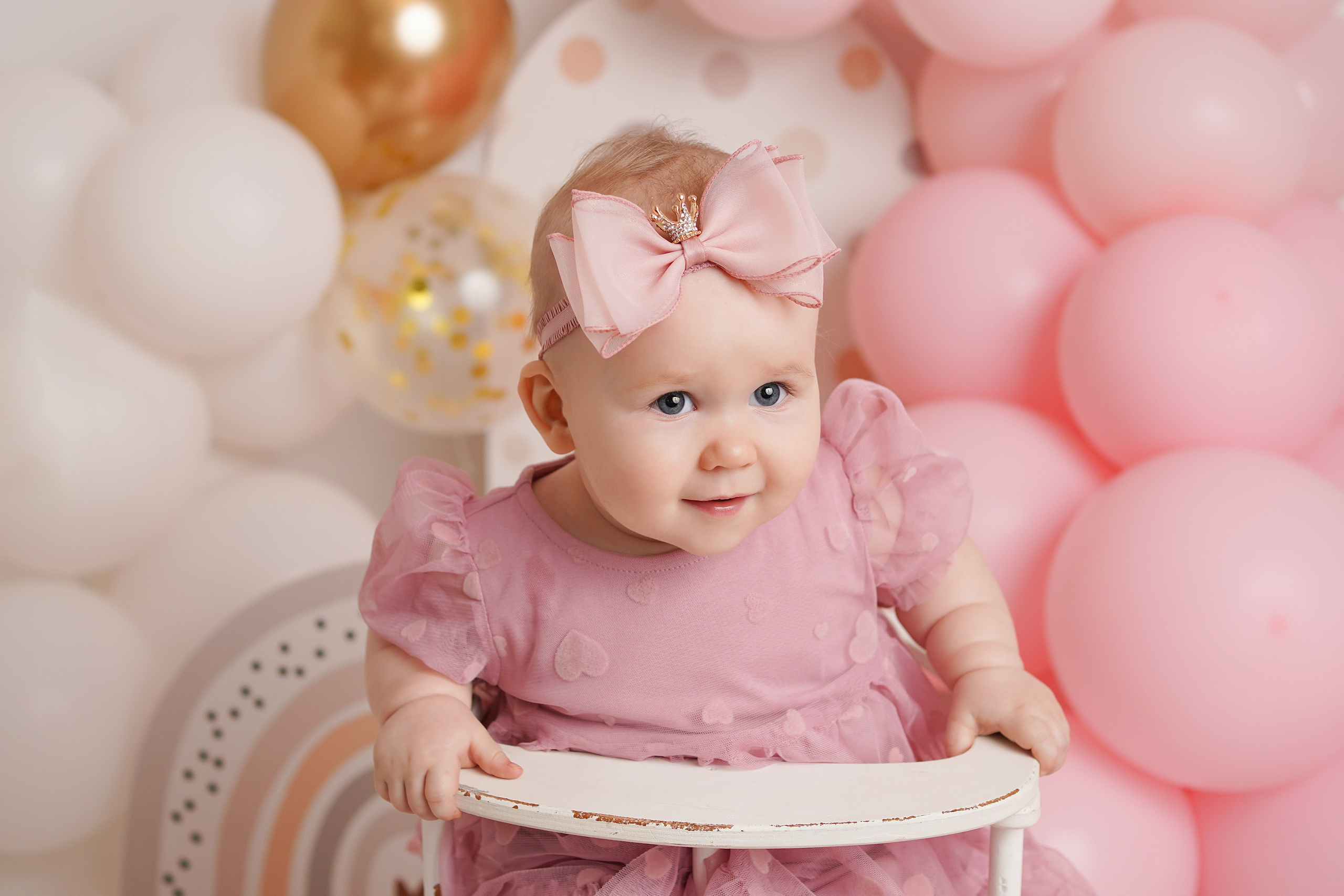 Малышка в нарядном розовом платье на фоне праздничной гирлянды из шаров.