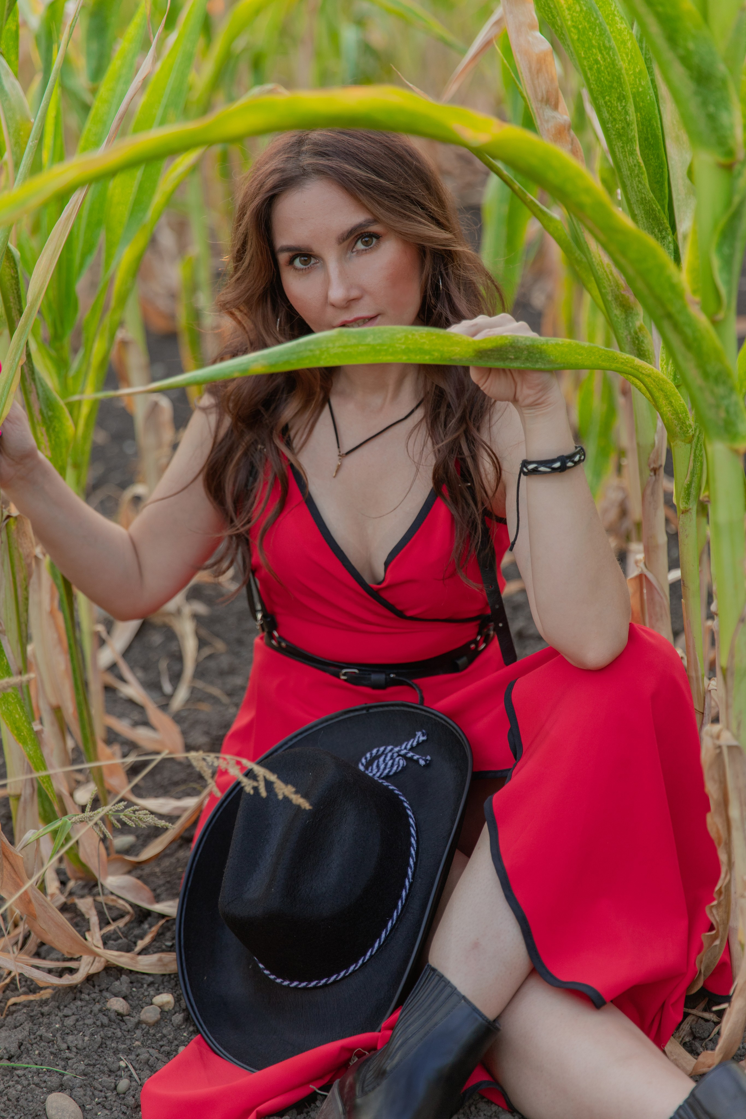  Летний пейзаж: девушка в красном платье со шляпой, сидит  на тропинке между рядами кукурузы, в окружении зелени