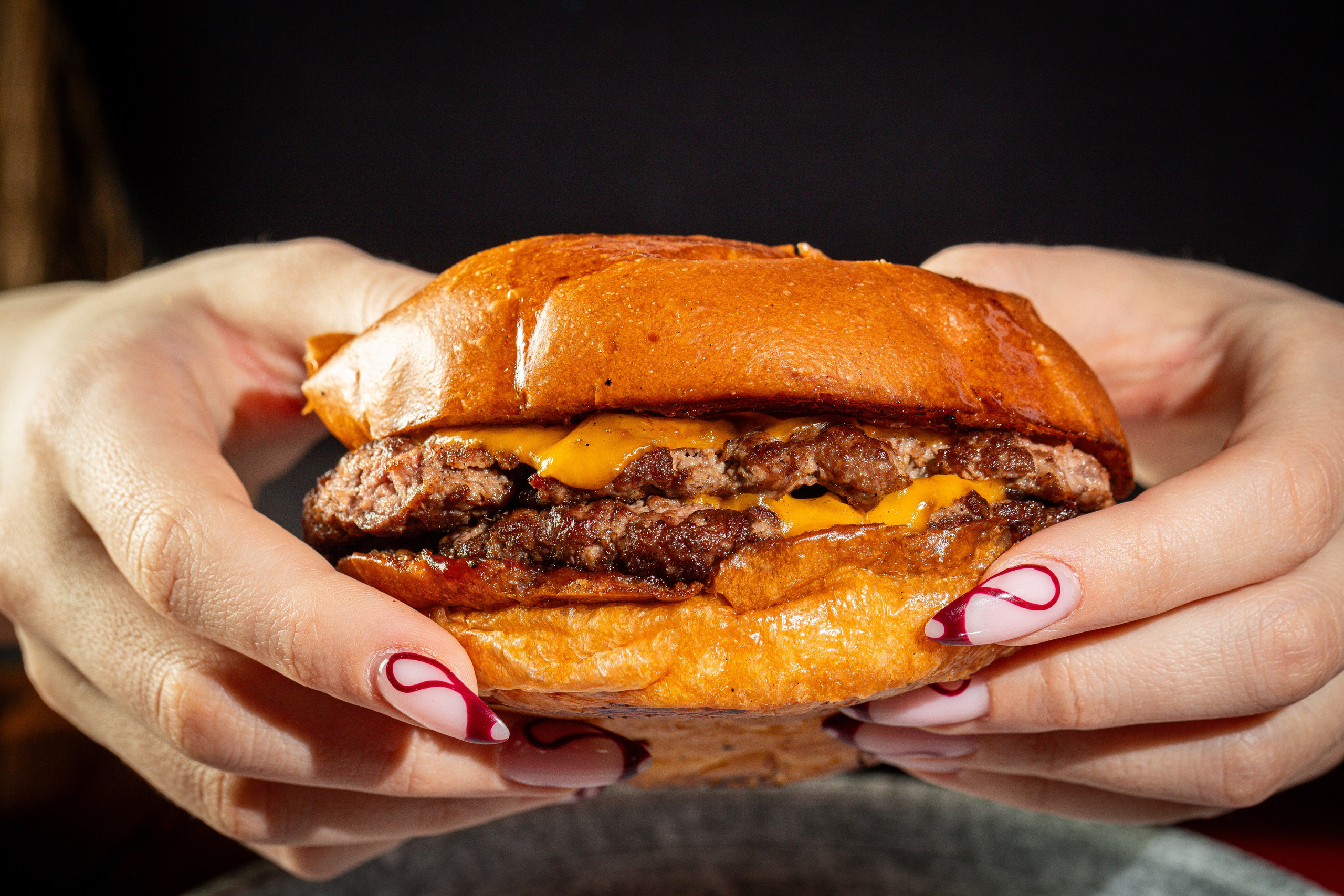 Смеш бургер с двумя котлетами из говядины с сыром чеддер в руках в девушки