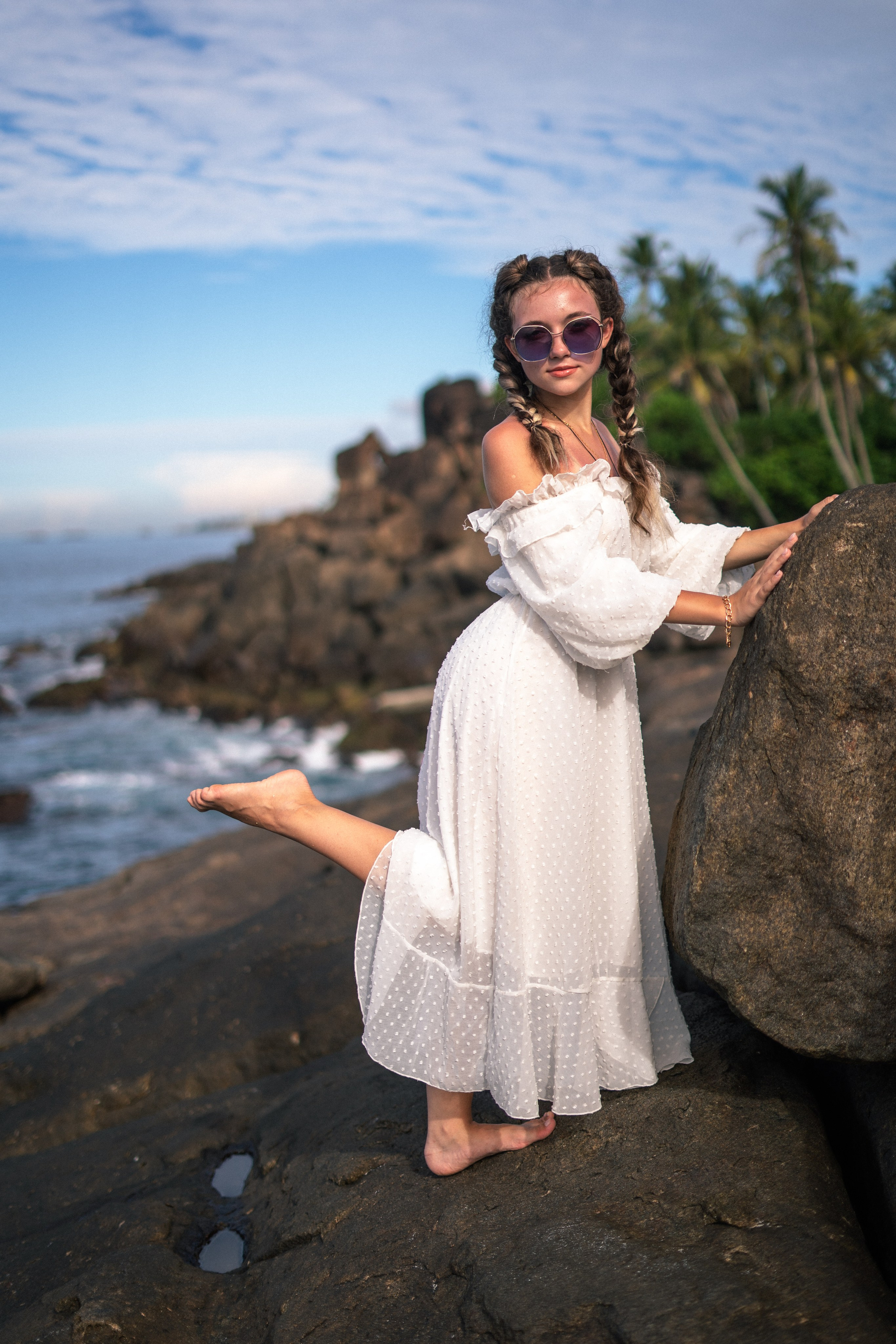 a young girl in a white dress and glasses against the backdrop of the vast ocean