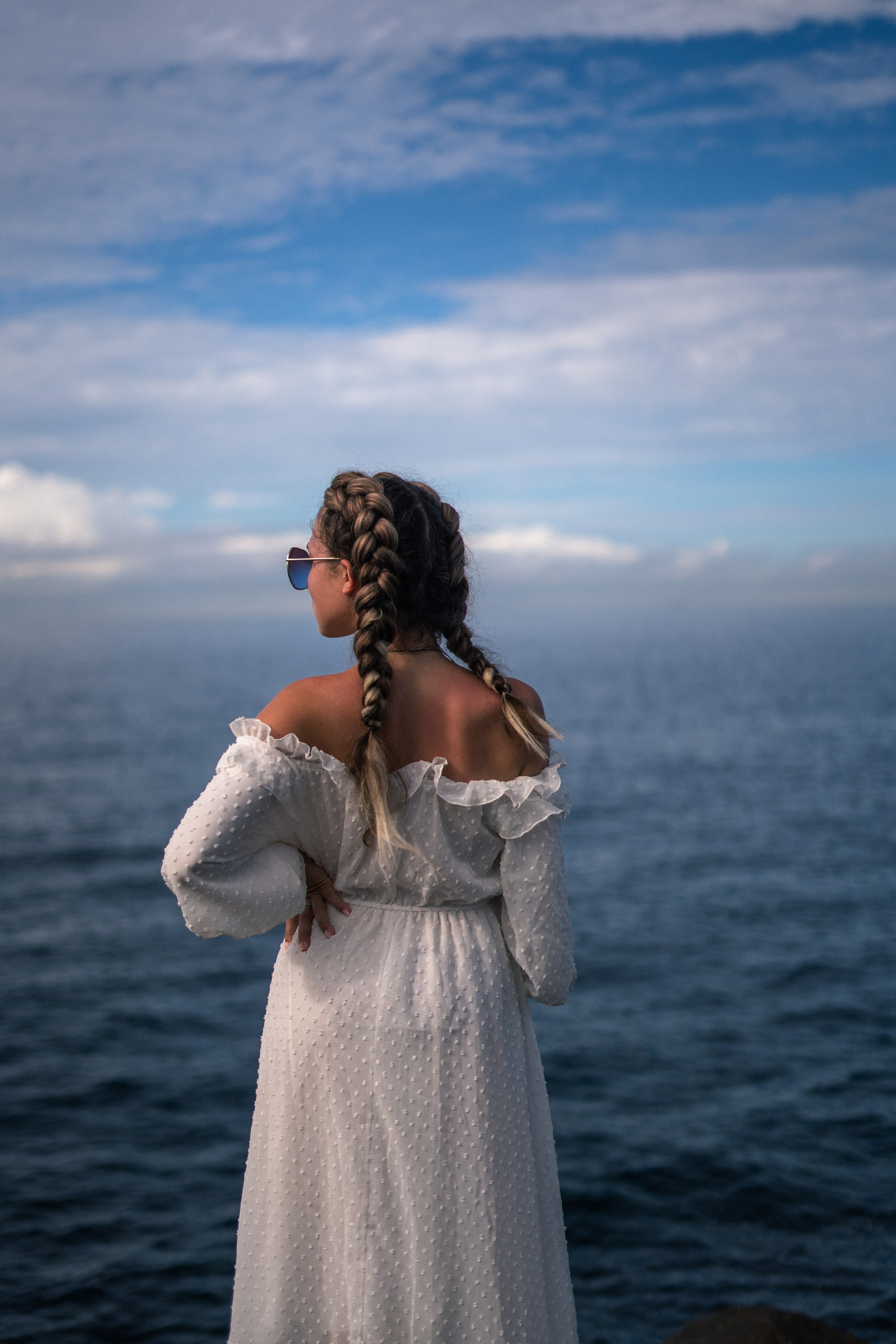 a girl in a white dress and glasses playing with water by the rocks