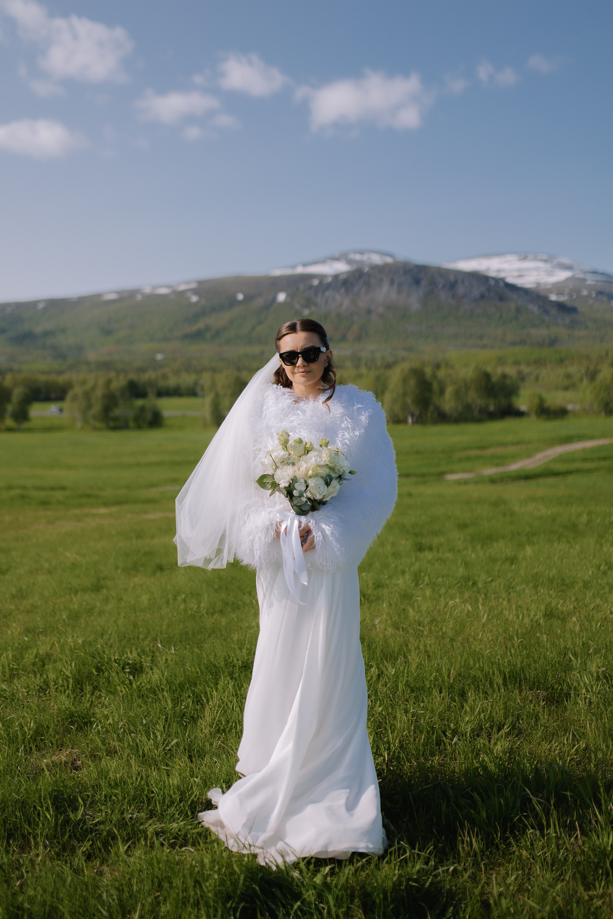 Девушка в элегантном свадебном платье идёт среди величественных горных вершин.