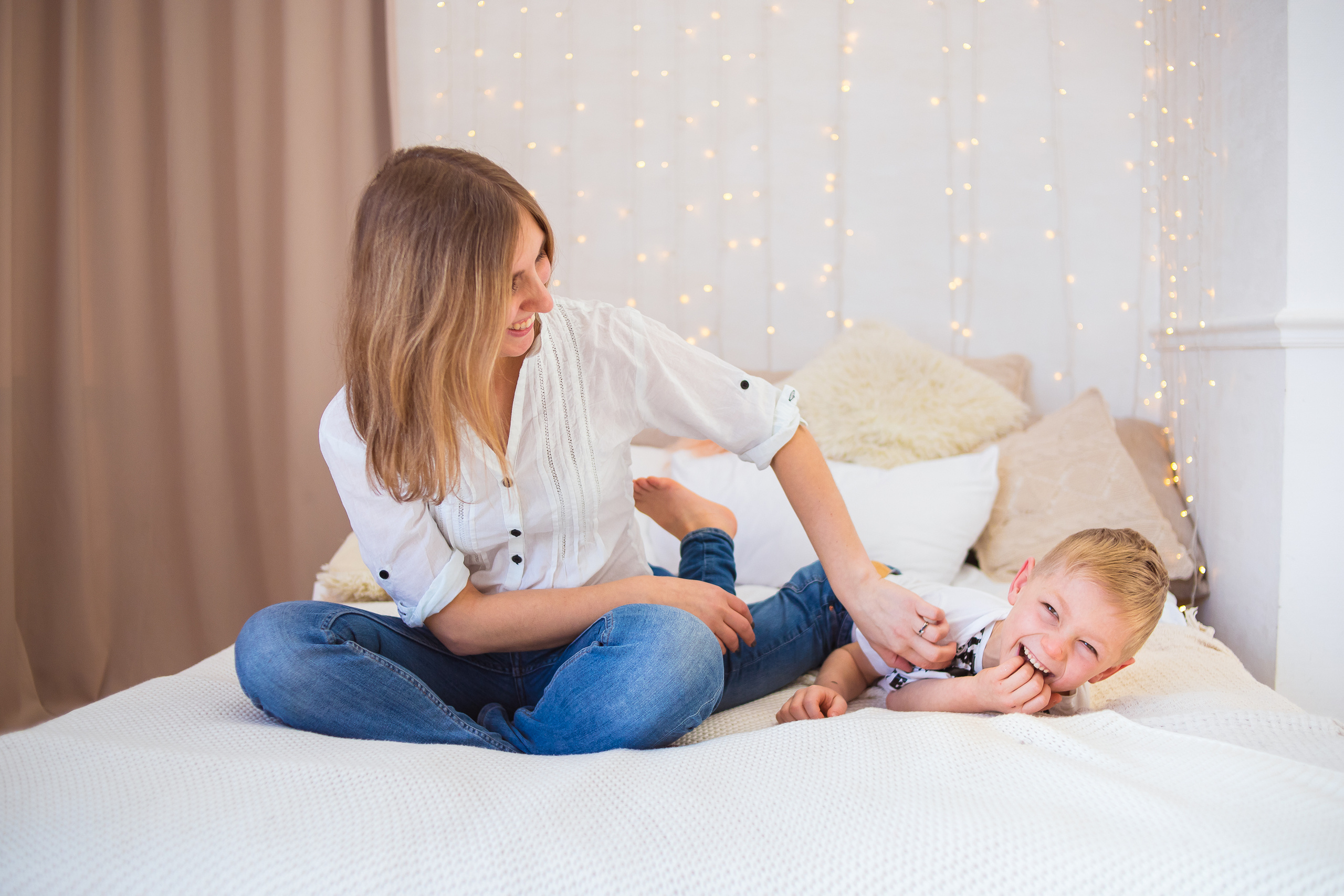 Мама и сын дурачатся на кровати. Мама щекочет сына. Задорный смех.