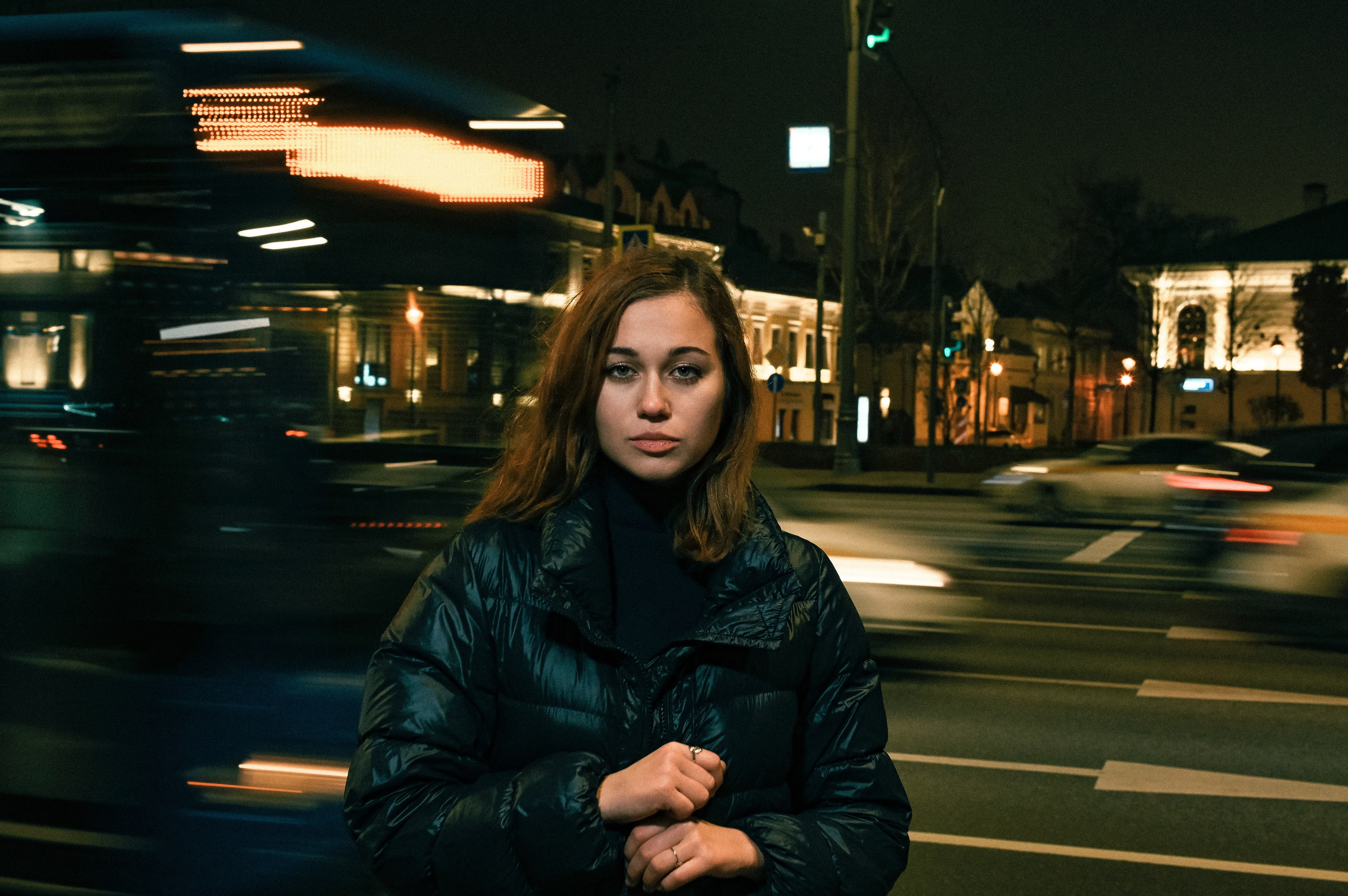 Ночной портрет девушки с волнистыми волосами в Москве, снятый на оживлённой дороге с эффектом движения транспорта.