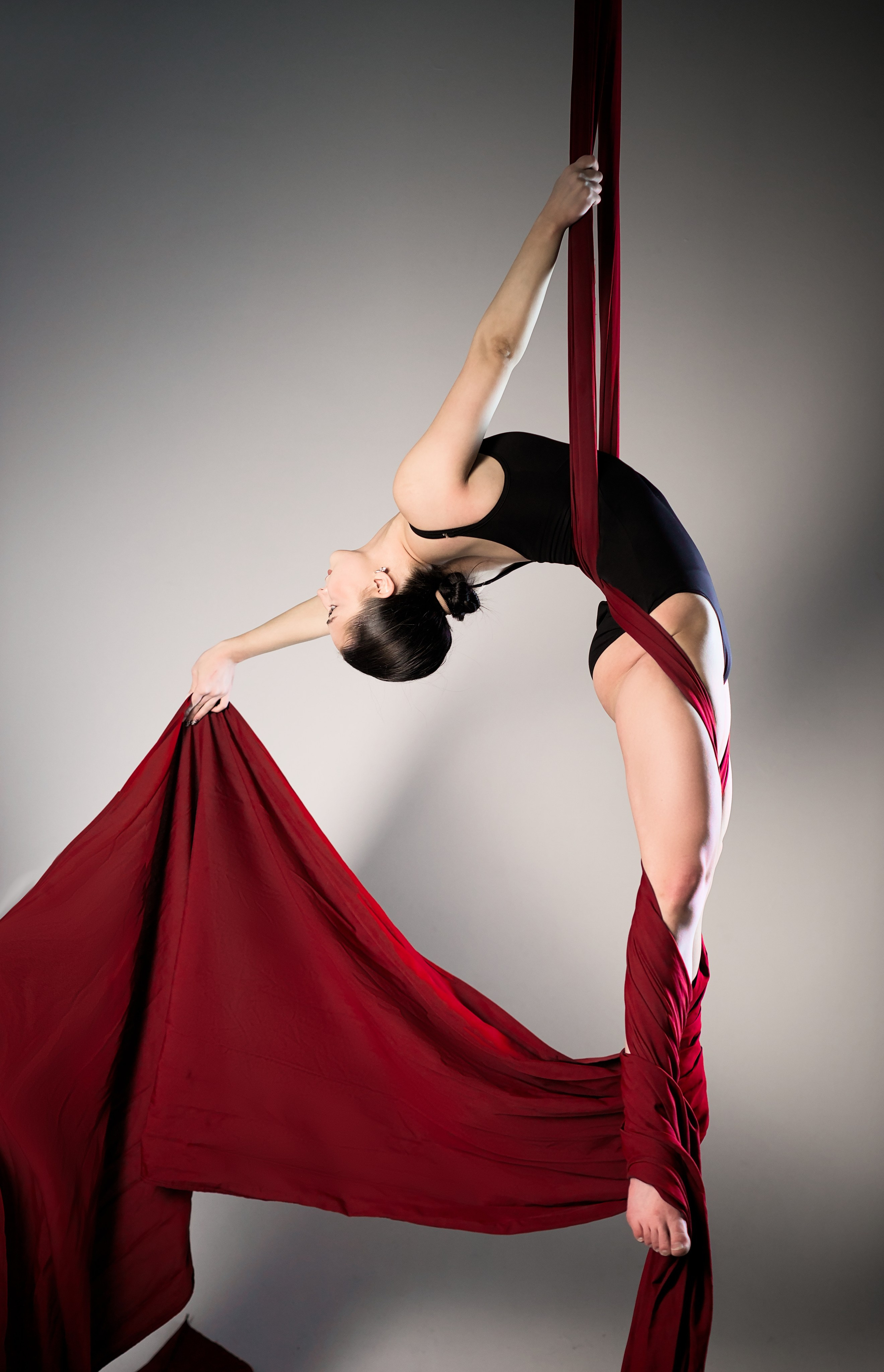 Эстетичная фигура гимнастки в обмотке на красных воздушных полотнах