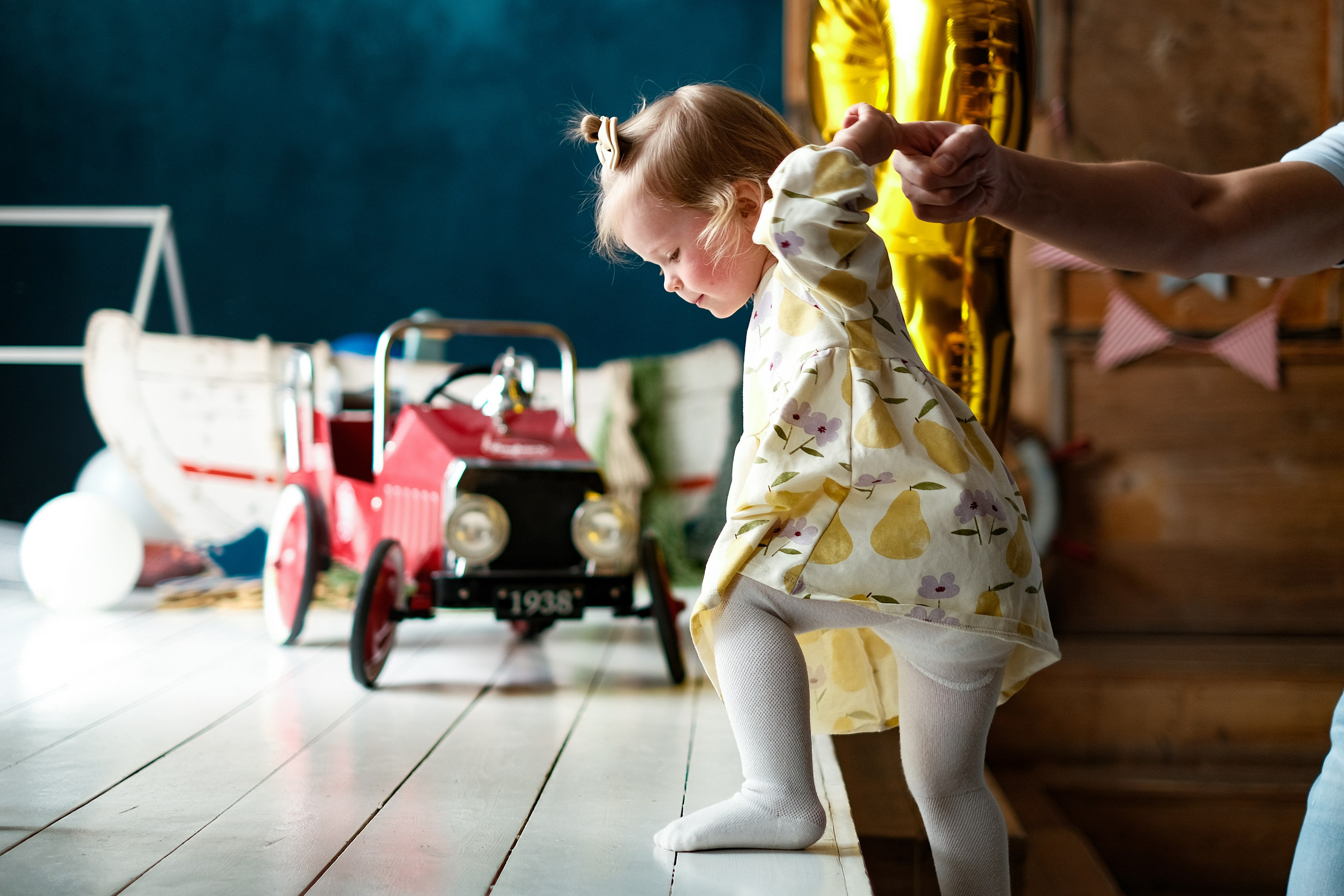 Маленькая девочка делает неуверенные шаги, держит папу за палец. Папа помогает дочке.