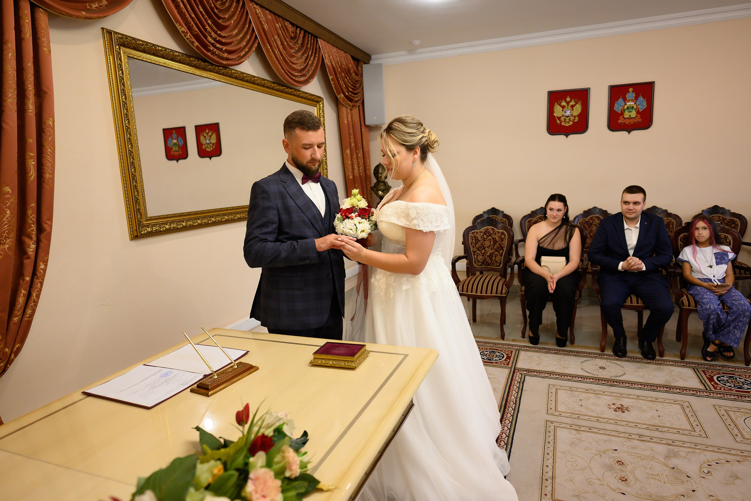 Жених и невеста обмениваются обручальными кольцами, свадебный фотограф запечатляет этот момент.