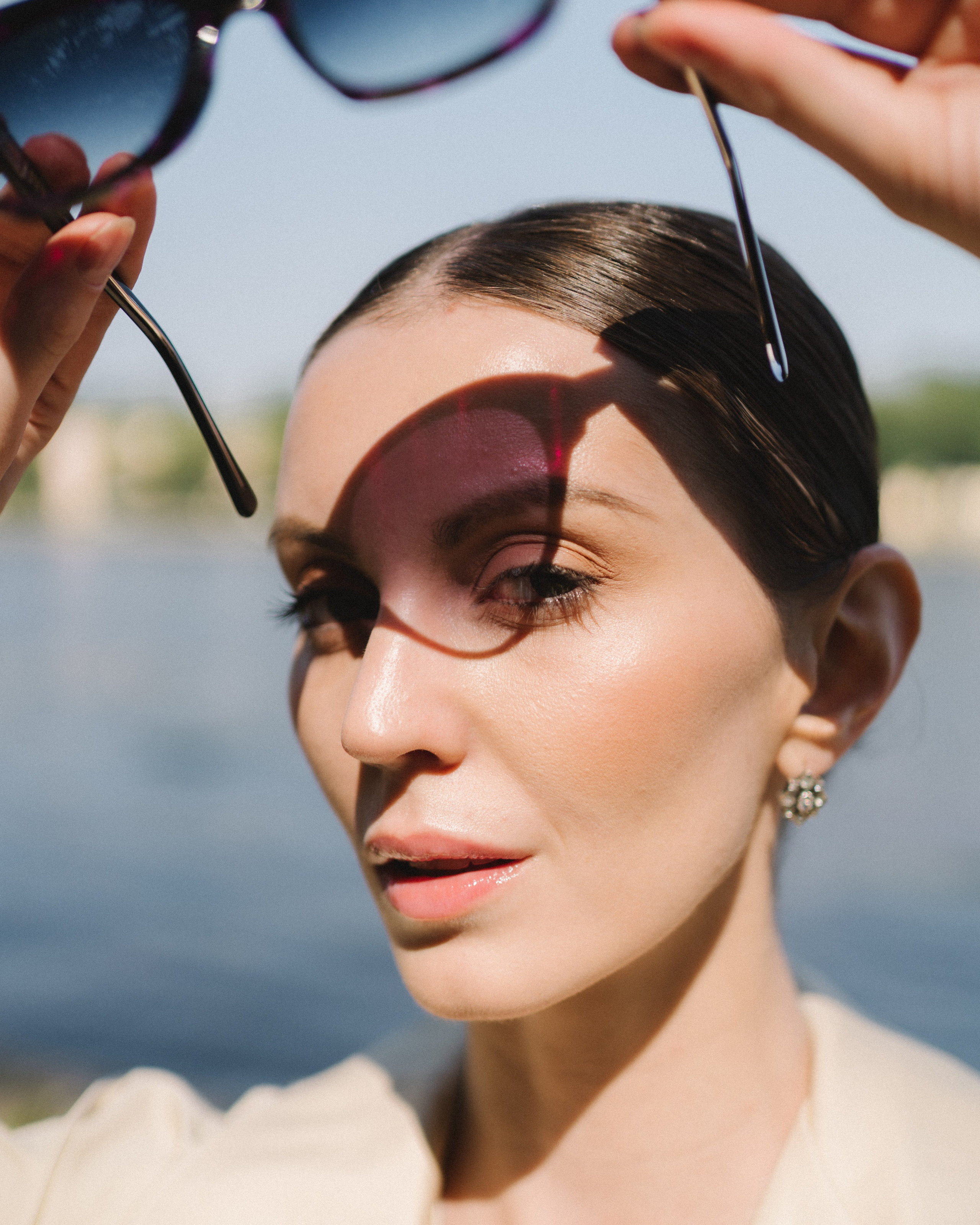 Креативный портрет девушки, которая держит в руках над собой очки, а тень от них падает на лицо.