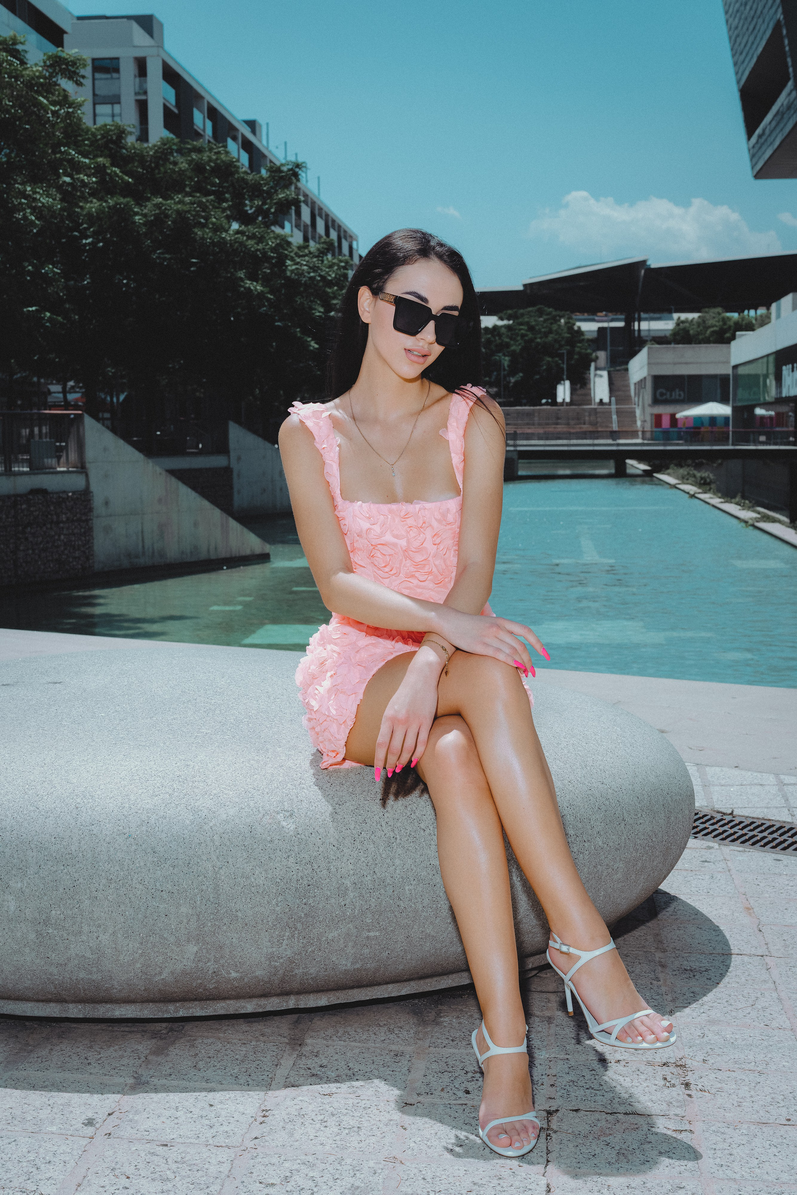 Woman in flowing blush dress standing on a sunny Barcelona balcony.