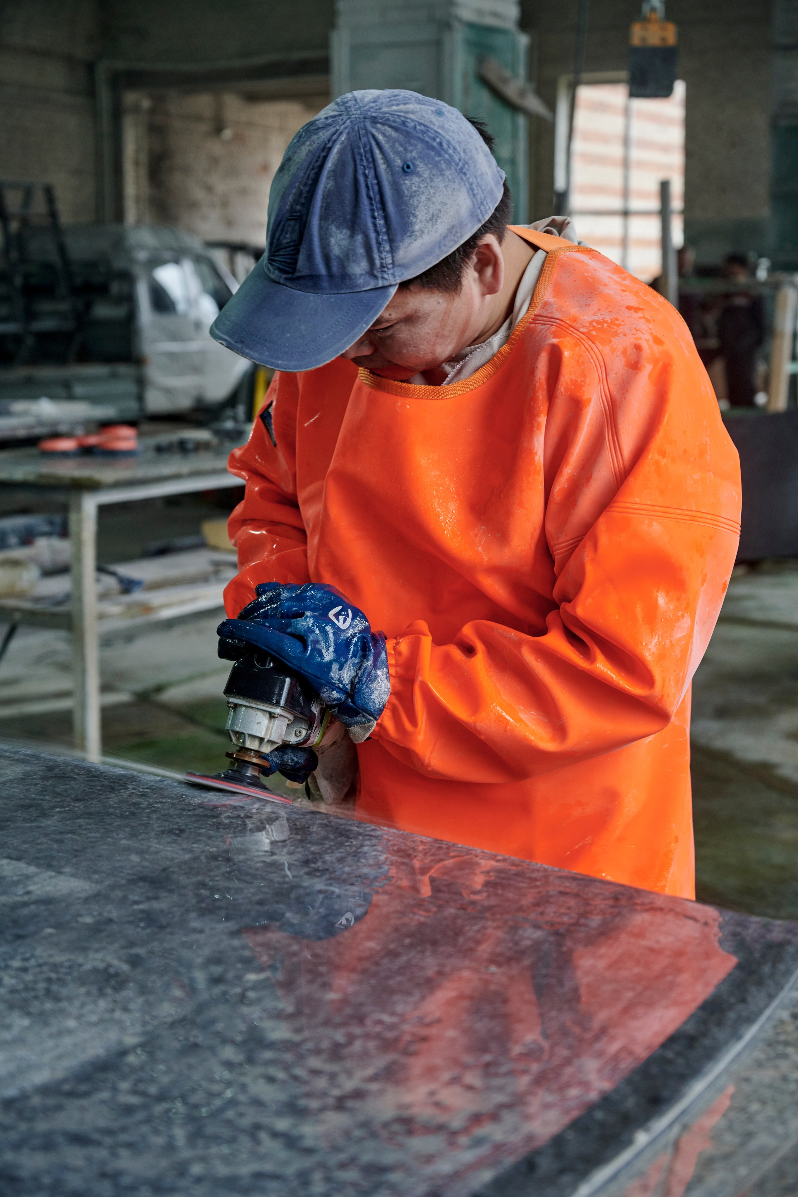 Рабочий в оранжевой куртке шлифует каменную плиту
