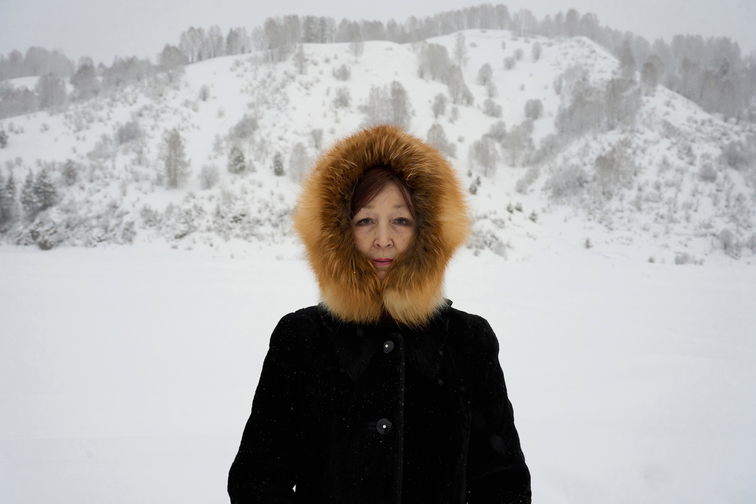 Lyubov Arbachakova stands against the backdrop of the taiga in the village of Ust-Kabyrza. She is a representative of a small indigenous people of Siberia — the Shors. Their population remains low due to the complex interplay of harsh social conditions, the isolation of their traditional mountain-taiga lifestyle, genetic intolerance to alcohol, and a high rate of suicides.