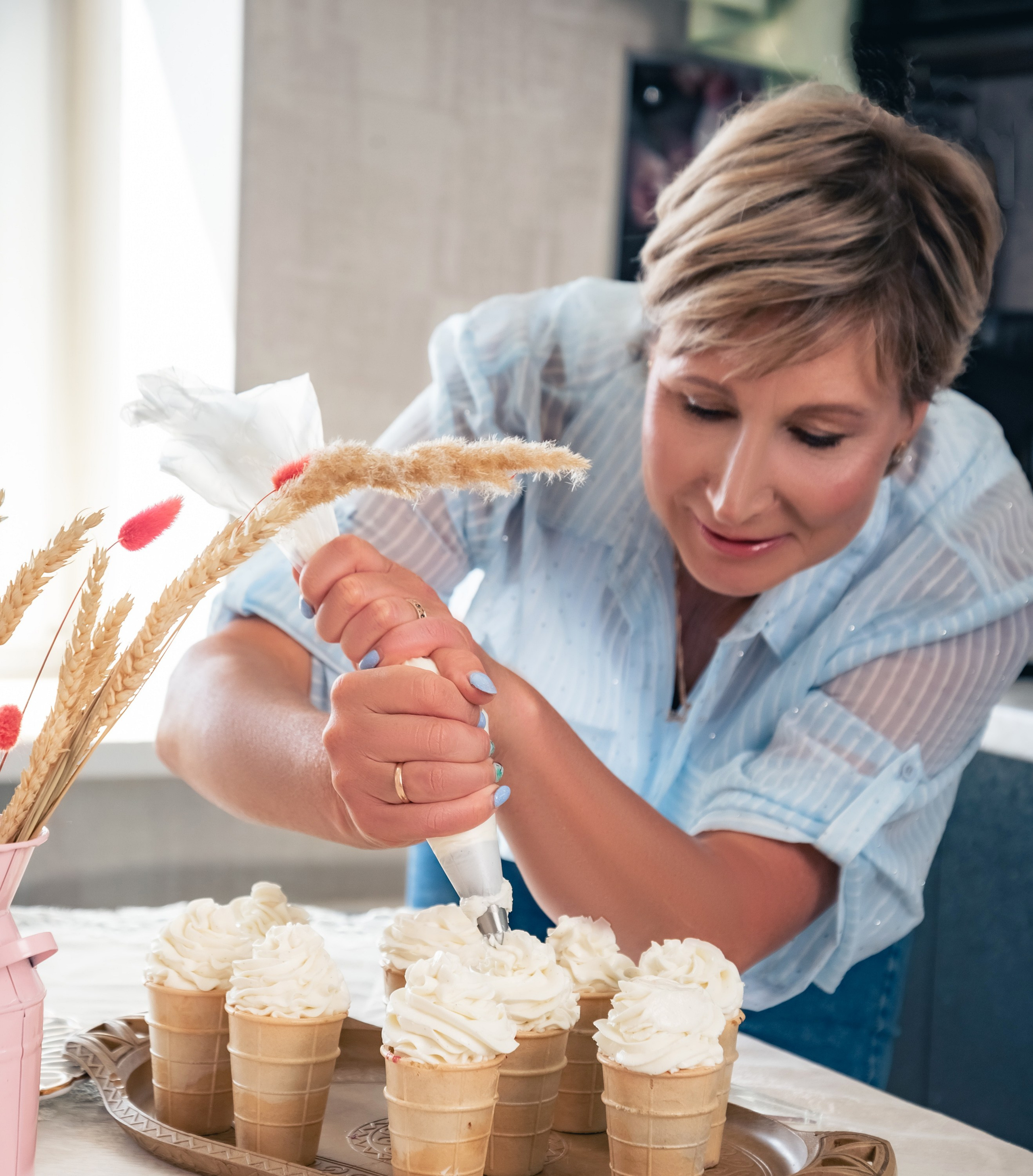 На фото женщина на кухне украшает кремом выпечку.