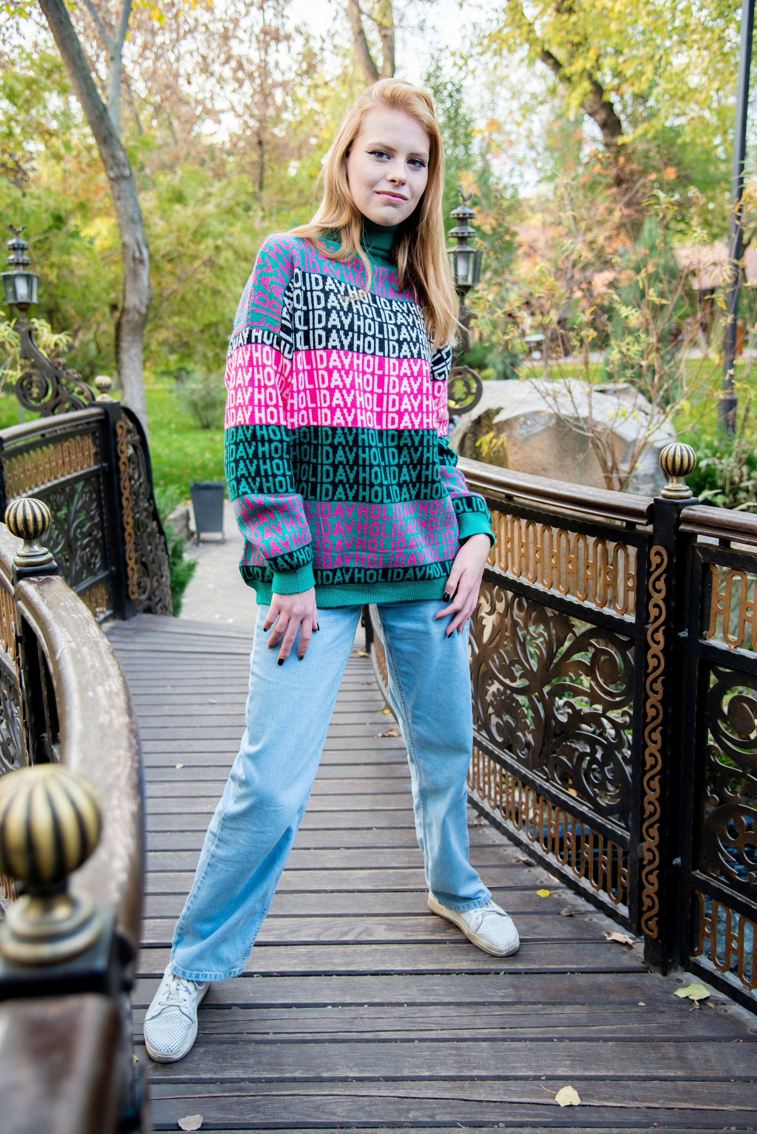 молодая девушка студентка. блондинка. длинные волосы. розово-зелёный свитер. парк Лога . осень на мостике