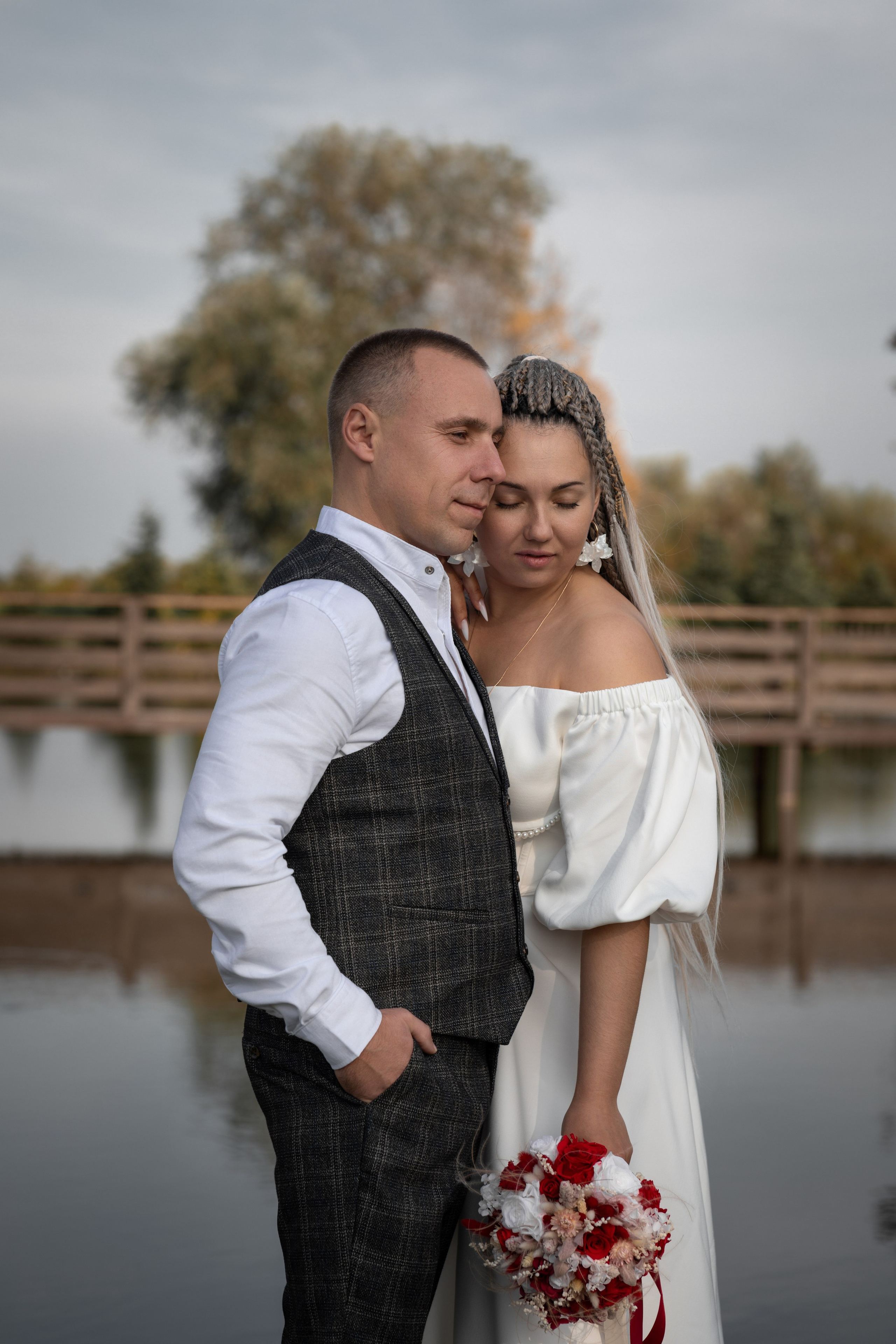Жених и невеста с букетом во время свадебной фотосессии у озера