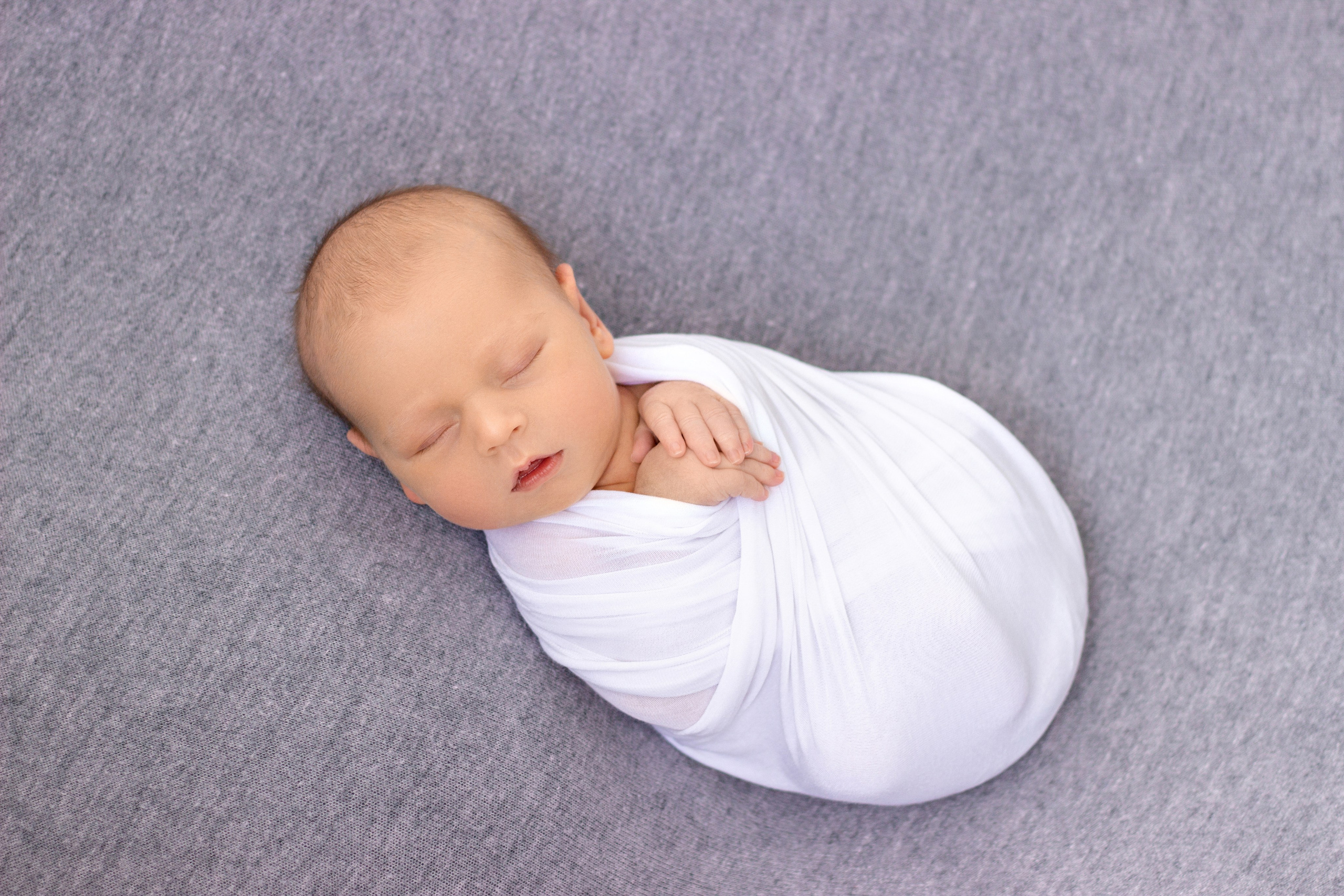съемка новорожденного мальчика с коликами беспокойным животиком в бело-серых тонах, после успокоения, укатанного в обмотку, с высунутыми ручками