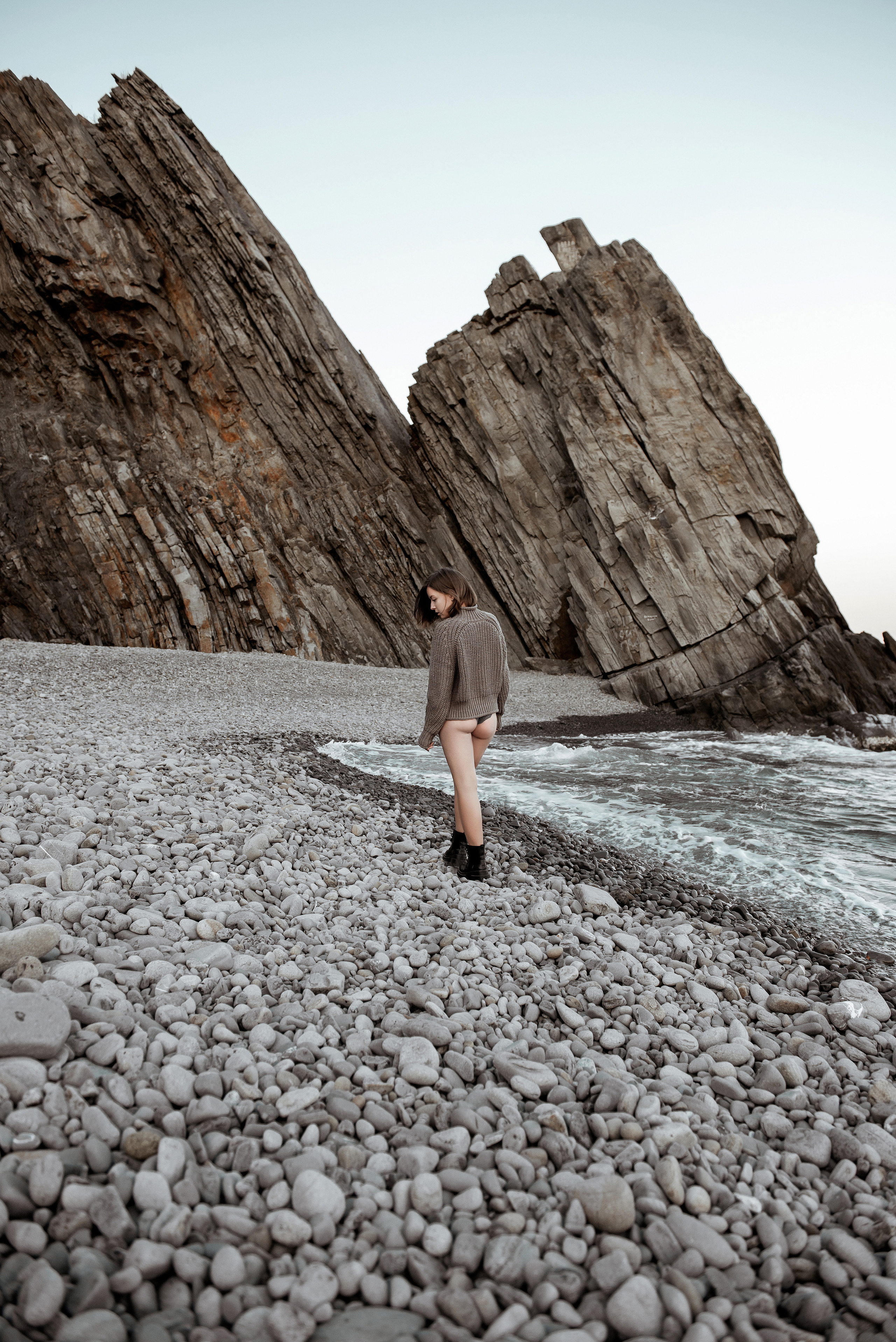 Девушка в трусиках и свитере идет по берегу моря