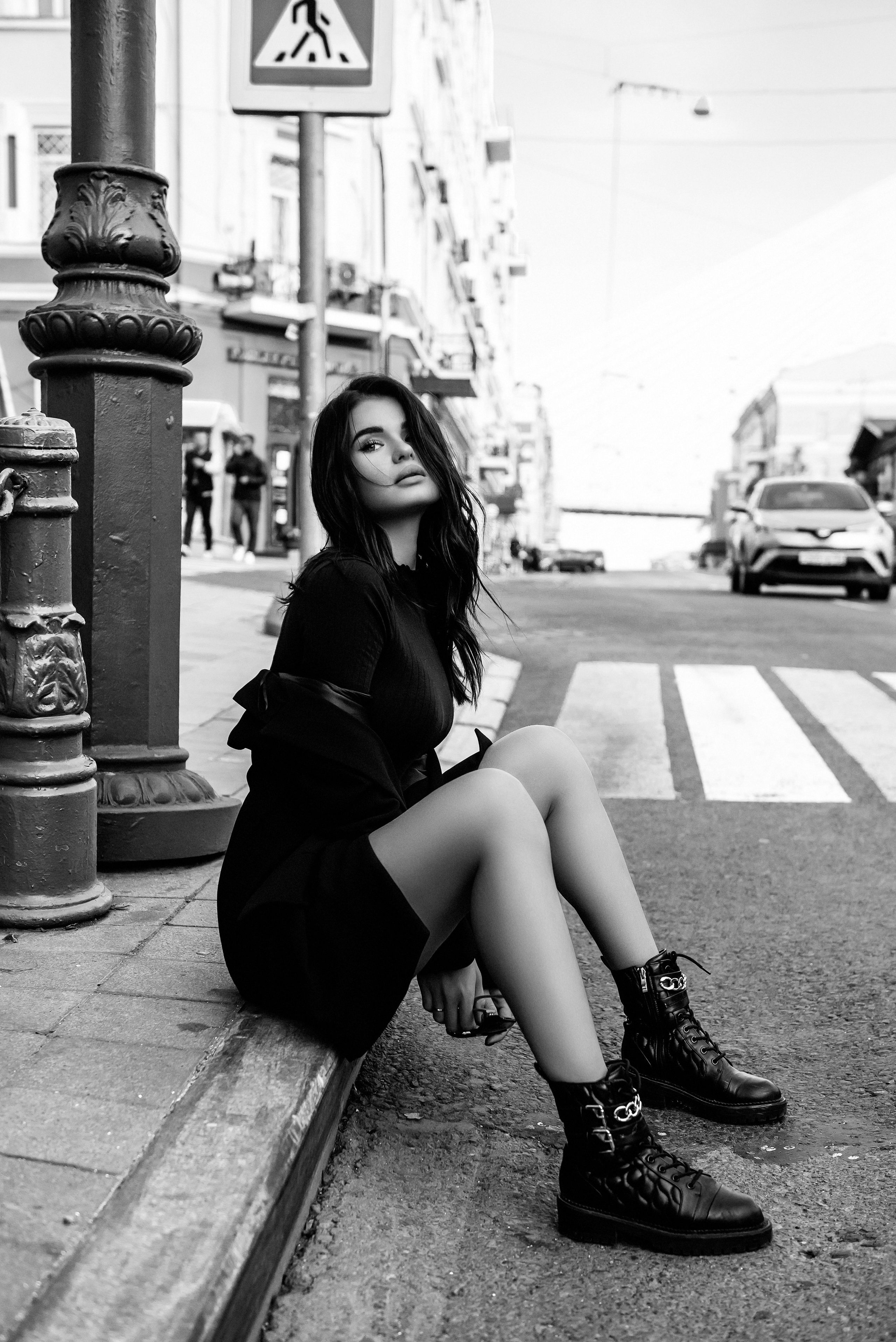 Девушка в пиджаке сидит на бордюре у дороги