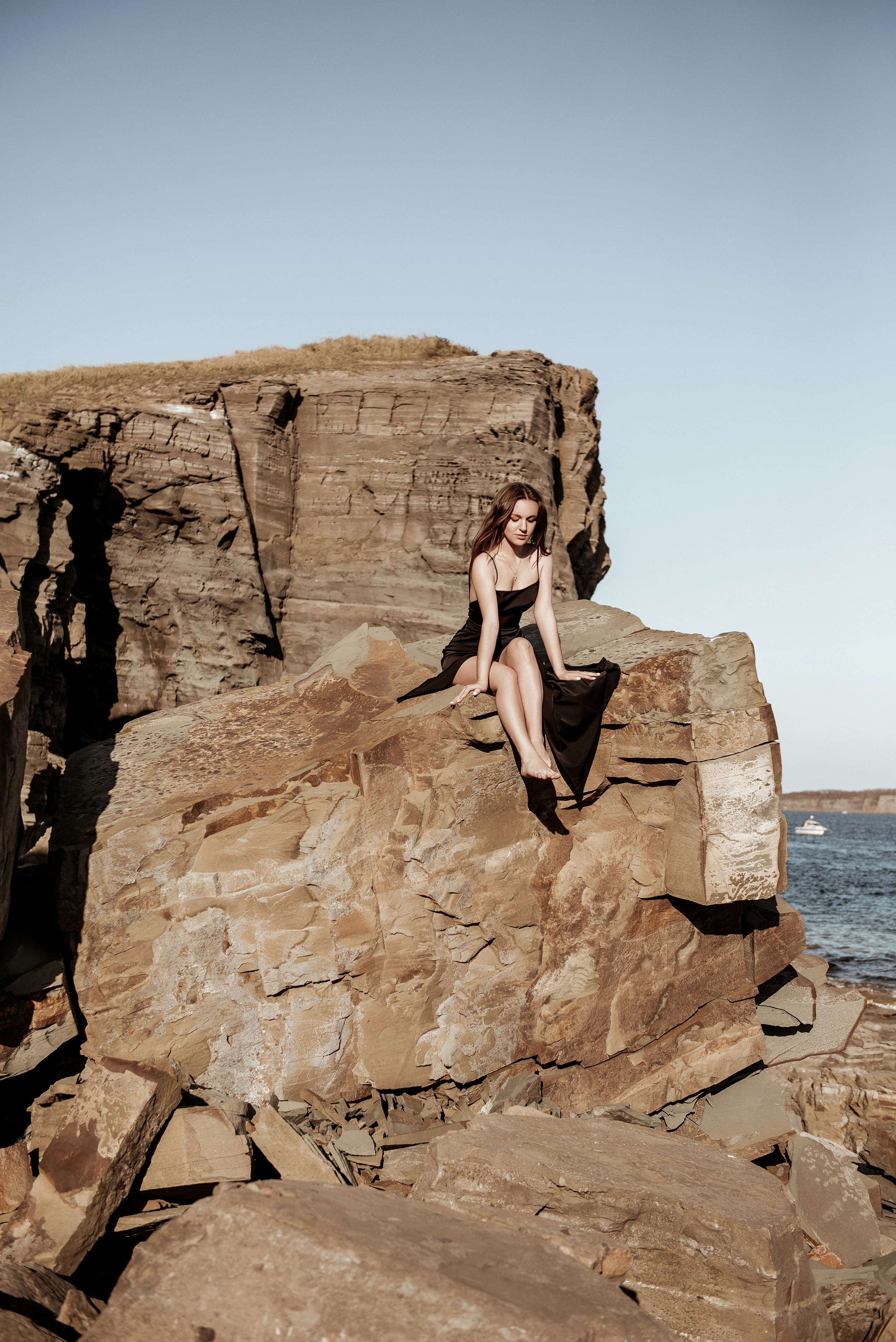 Девушка сидит на высокой скале на море