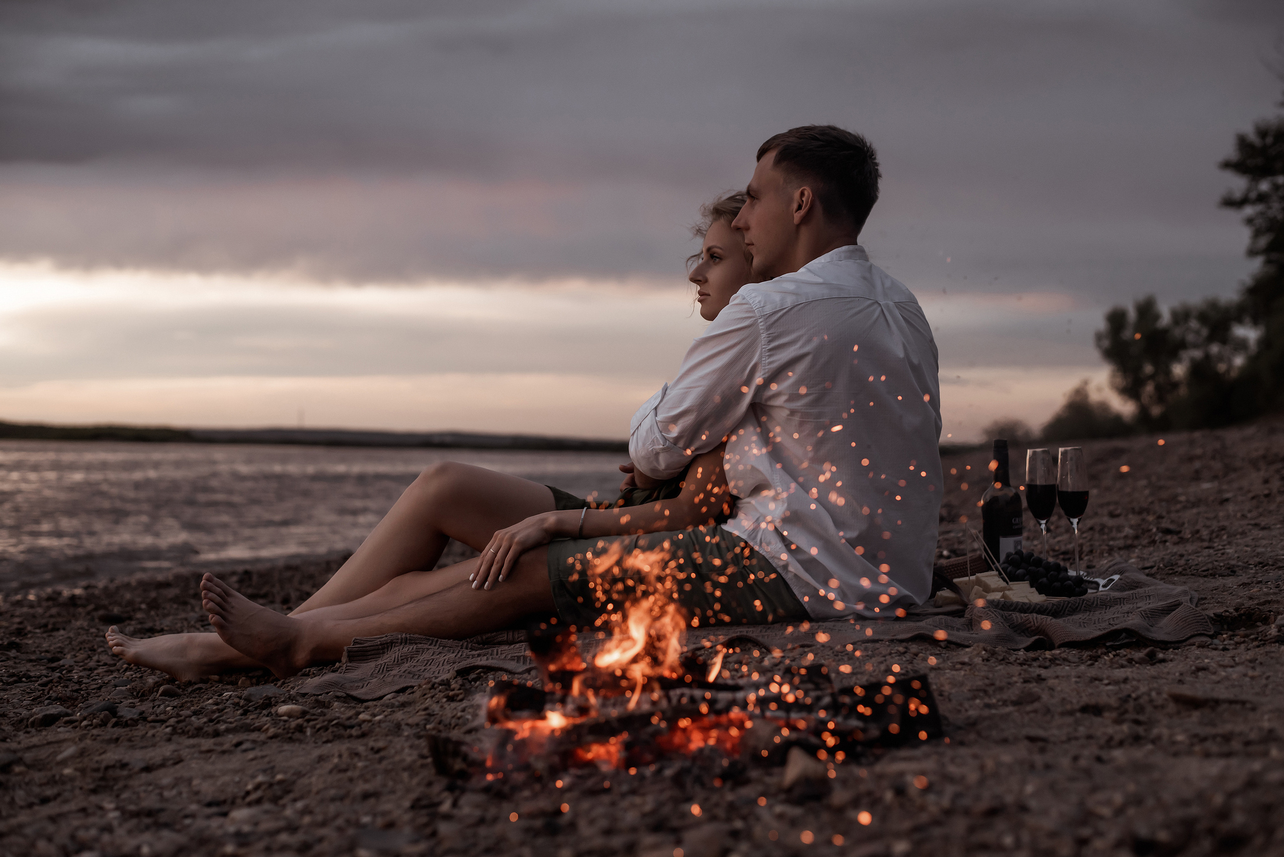 Пара обнимается на берегу реки. Фотография на Love Story  с костром
