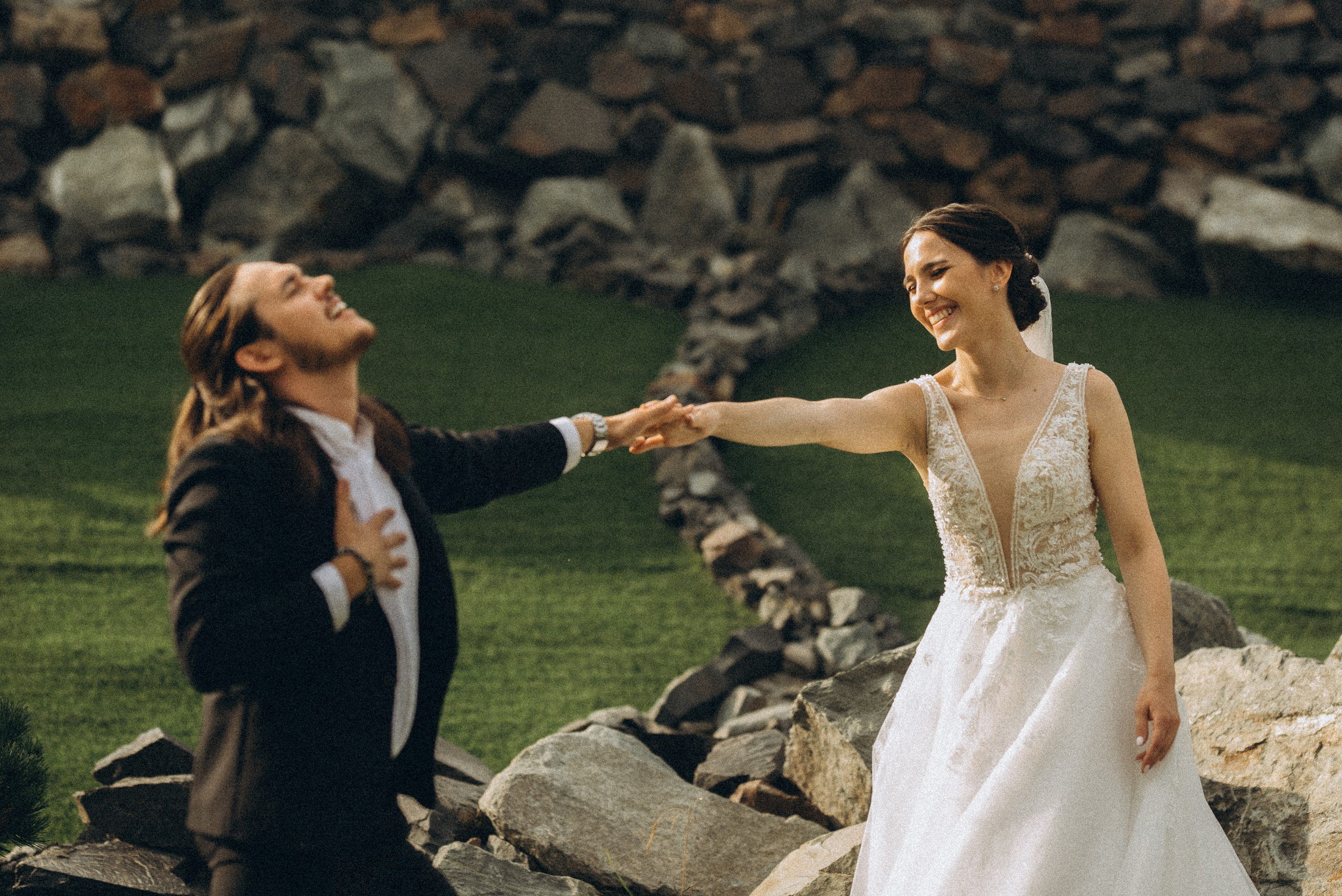 Живой и динамичный кадр: смеющаяся невеста и жених в движении на фоне камней.
