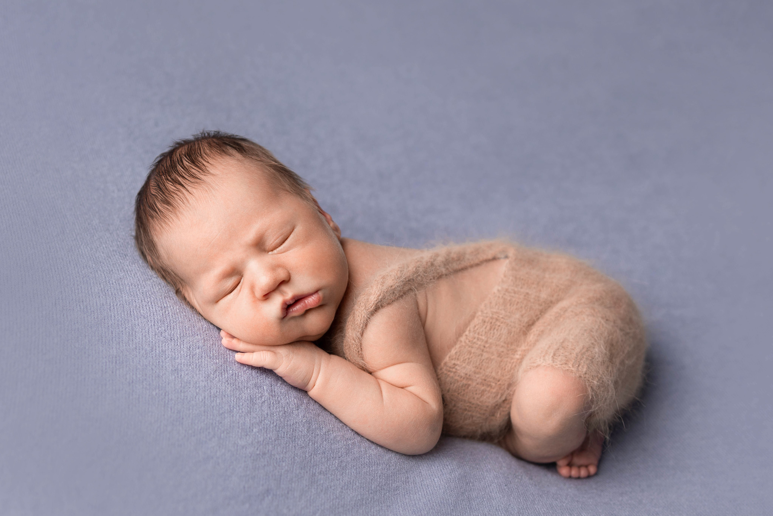 Спящий новорожденный в бежевом теплом конверте на голубом фоне.