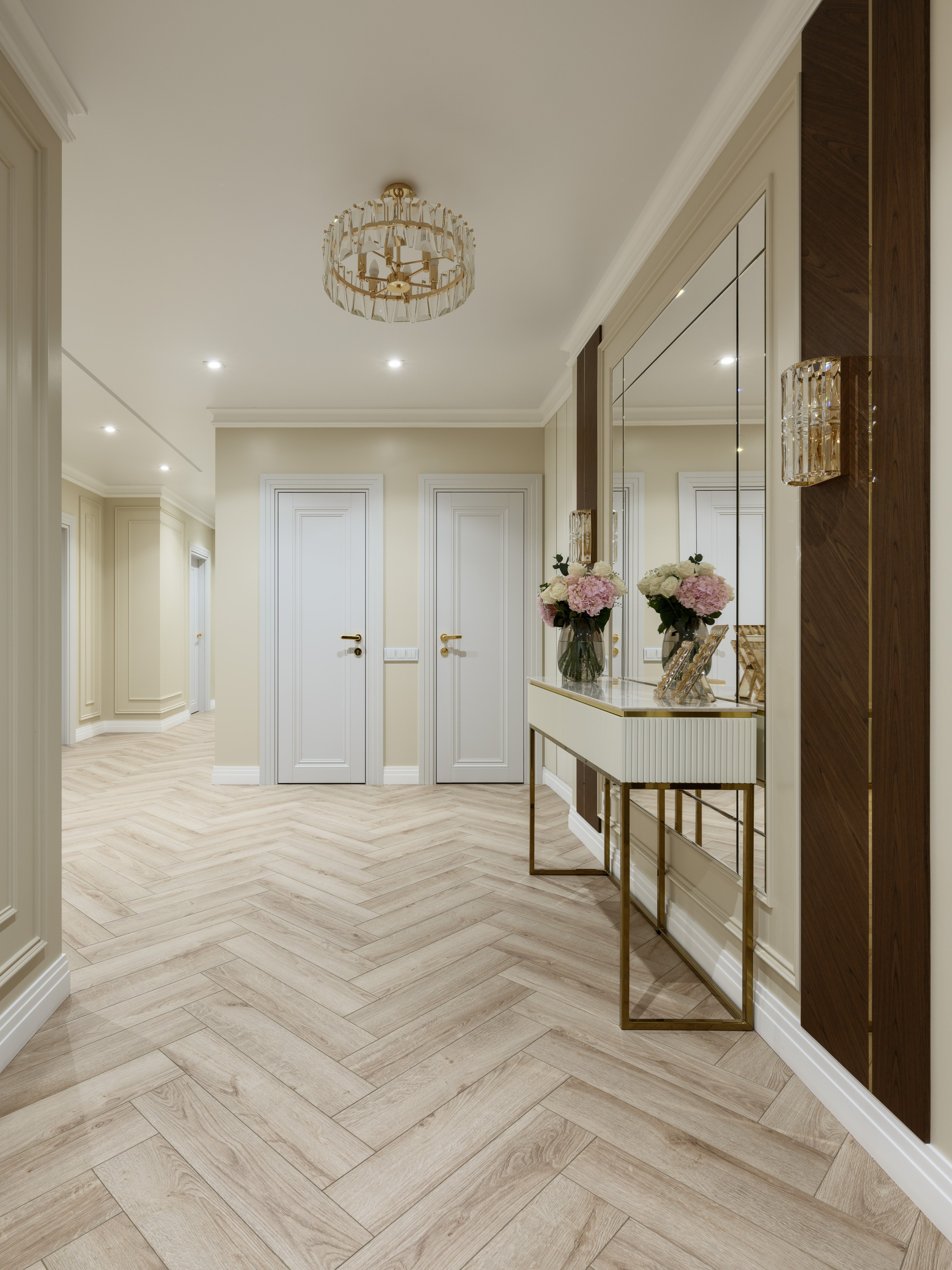 Просторный светлый холл с паркетом ёлочкой, консолью с зеркалом и цветочной композицией. Стены в молочных тонах, потолочный светильник с хрусталём. Дизайн разработан Евгенией Ермошиной, фотограф Сергей Денисенко.