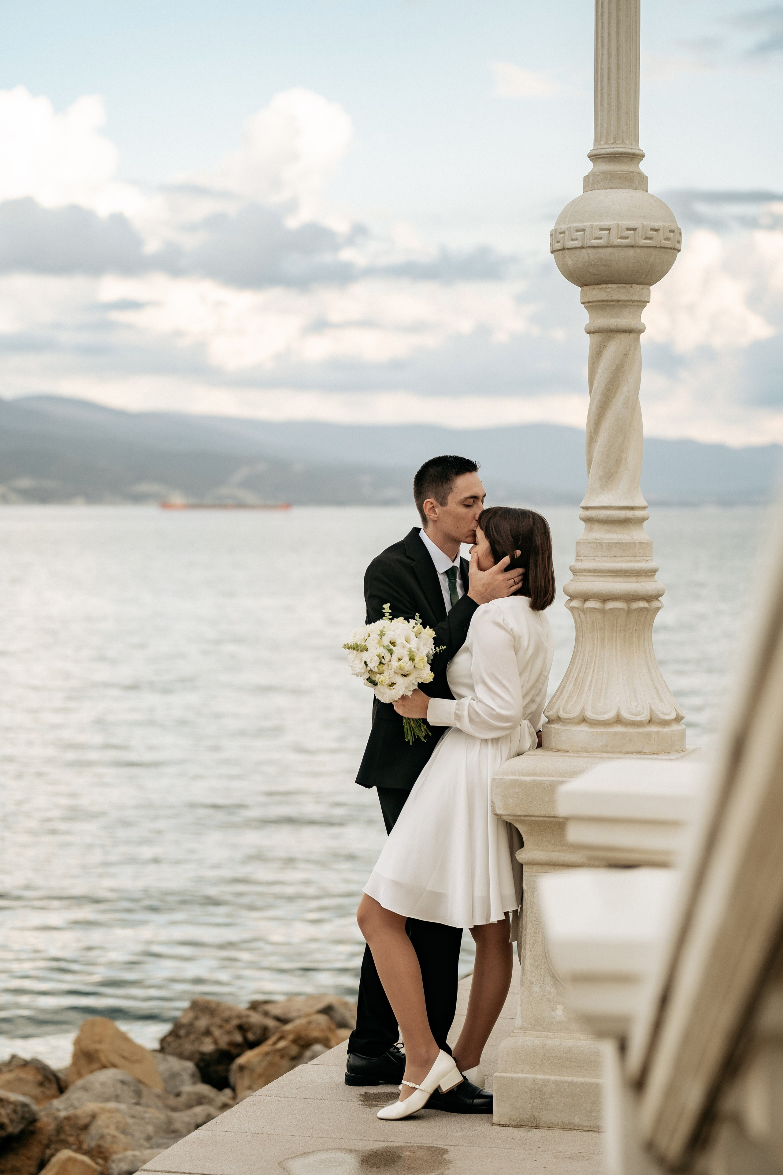 Свадьба в Новороссийске у моря. Крупный план с переплетенными руками и обручальными кольцами на фоне морского пейзажа.