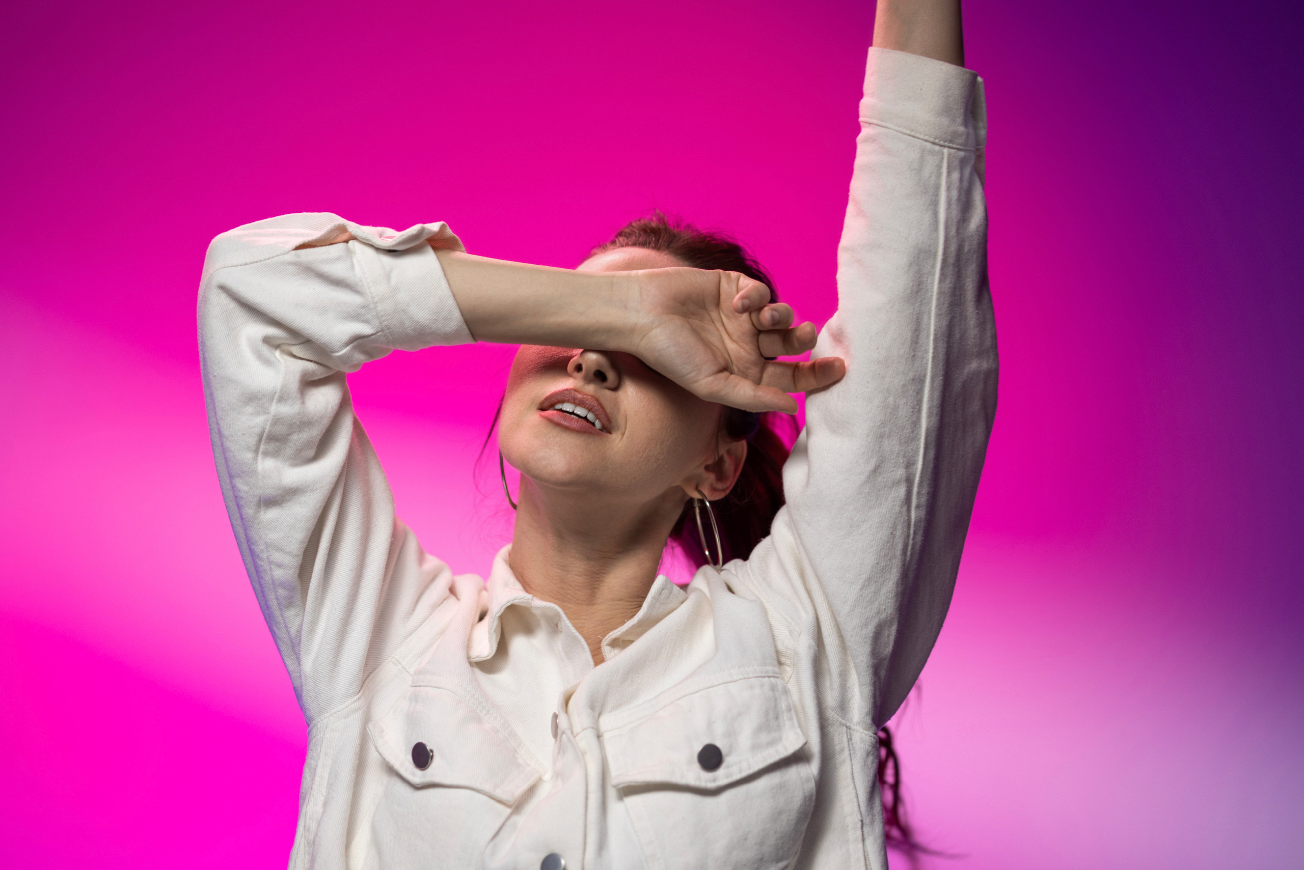 Девушка модельной внешности в белой джинсовой куртке на фиолетово-розовом фоне