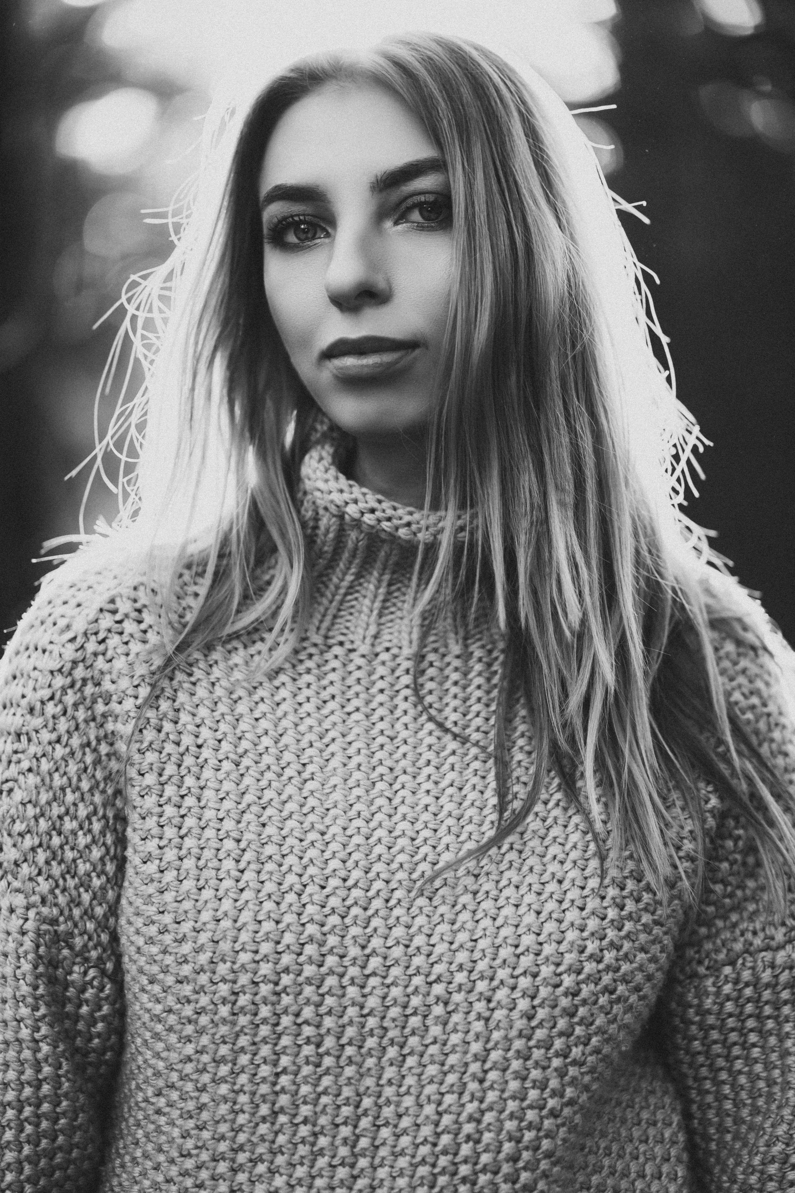 Девушка в вязанном свитере с горлом, мило улыбается и смотрит в камеру