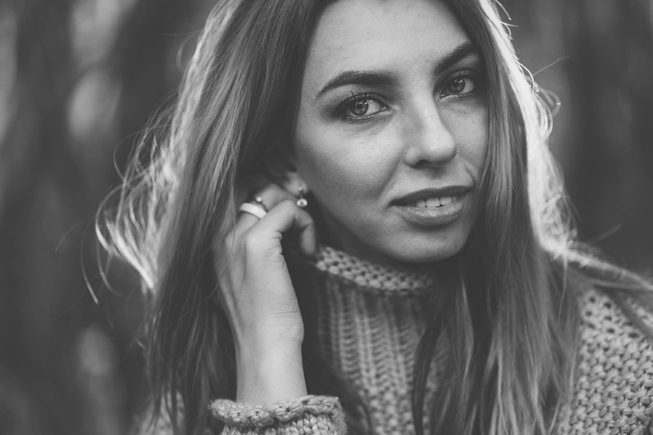 Девушка в вязанном свитере с горлом, улыбается держа правую руку у лица и поправляя ворот на свитере