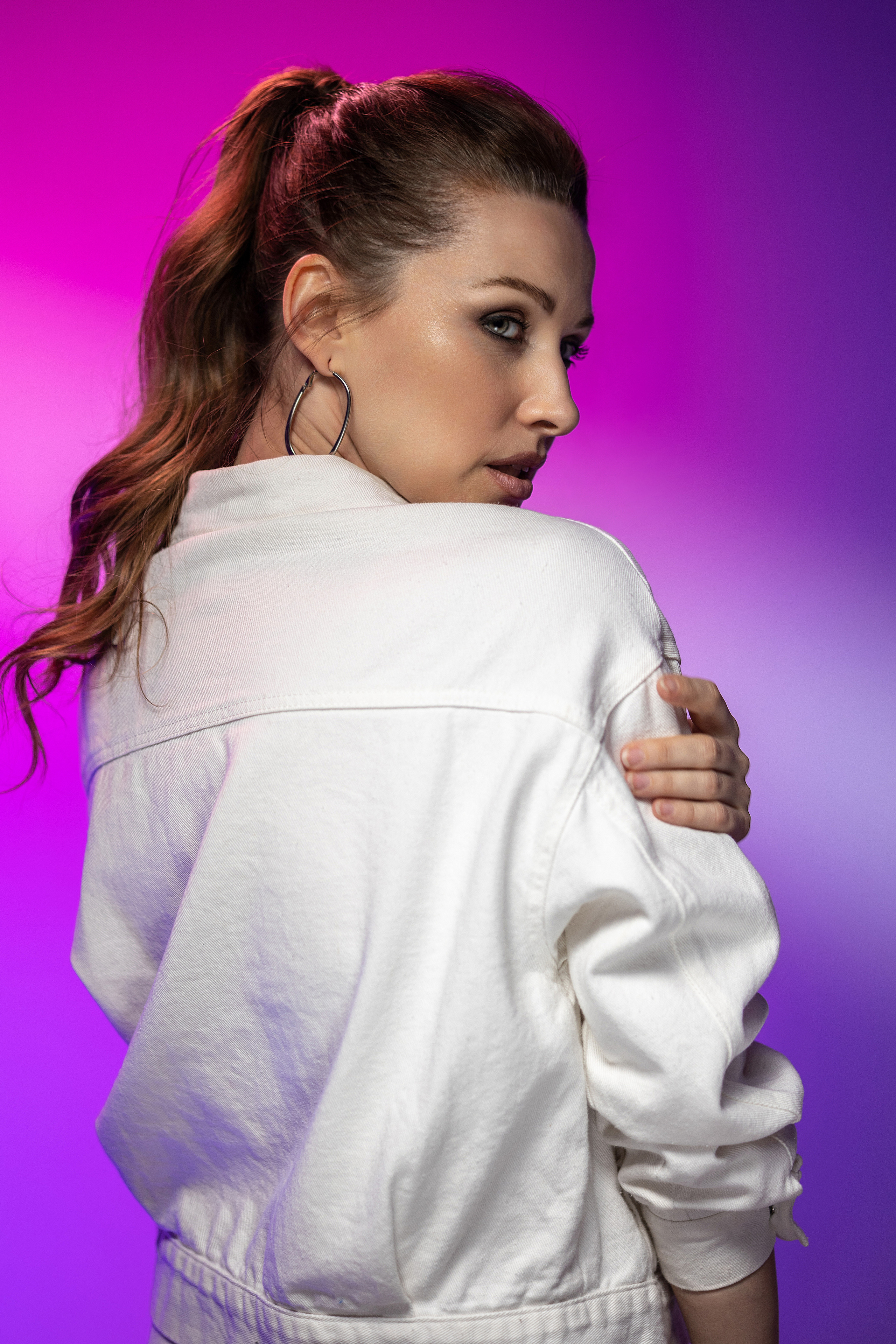 Девушка модельной внешности в белой джинсовой куртке на фиолетово-розовом фоне