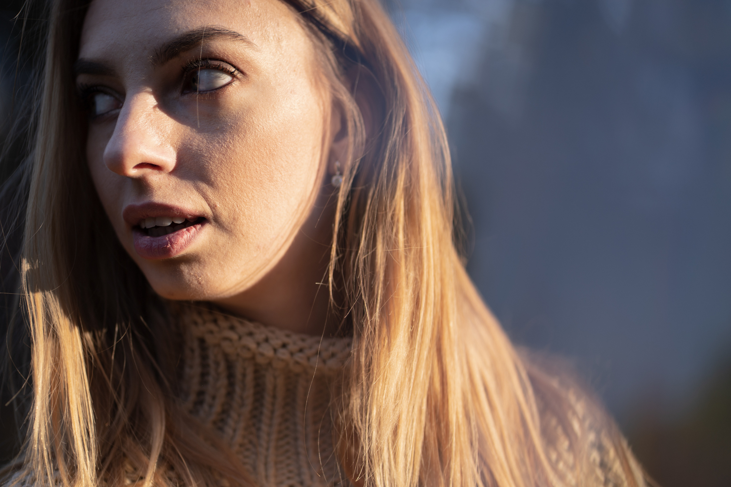 Девушка в вязанном свитере с горлом, с интересом смотрит на объект вне кадра