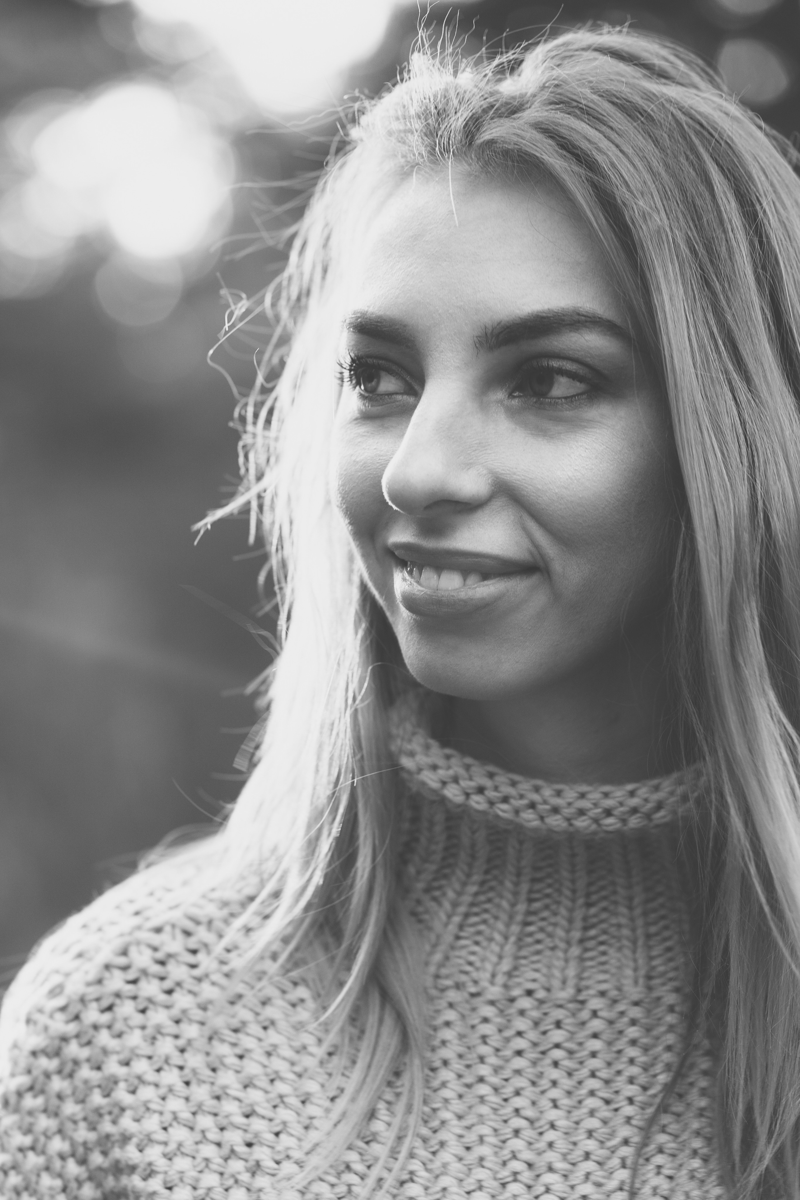 Девушка в вязанном свитере с горлом, мило улыбается и смотрит не в камеру