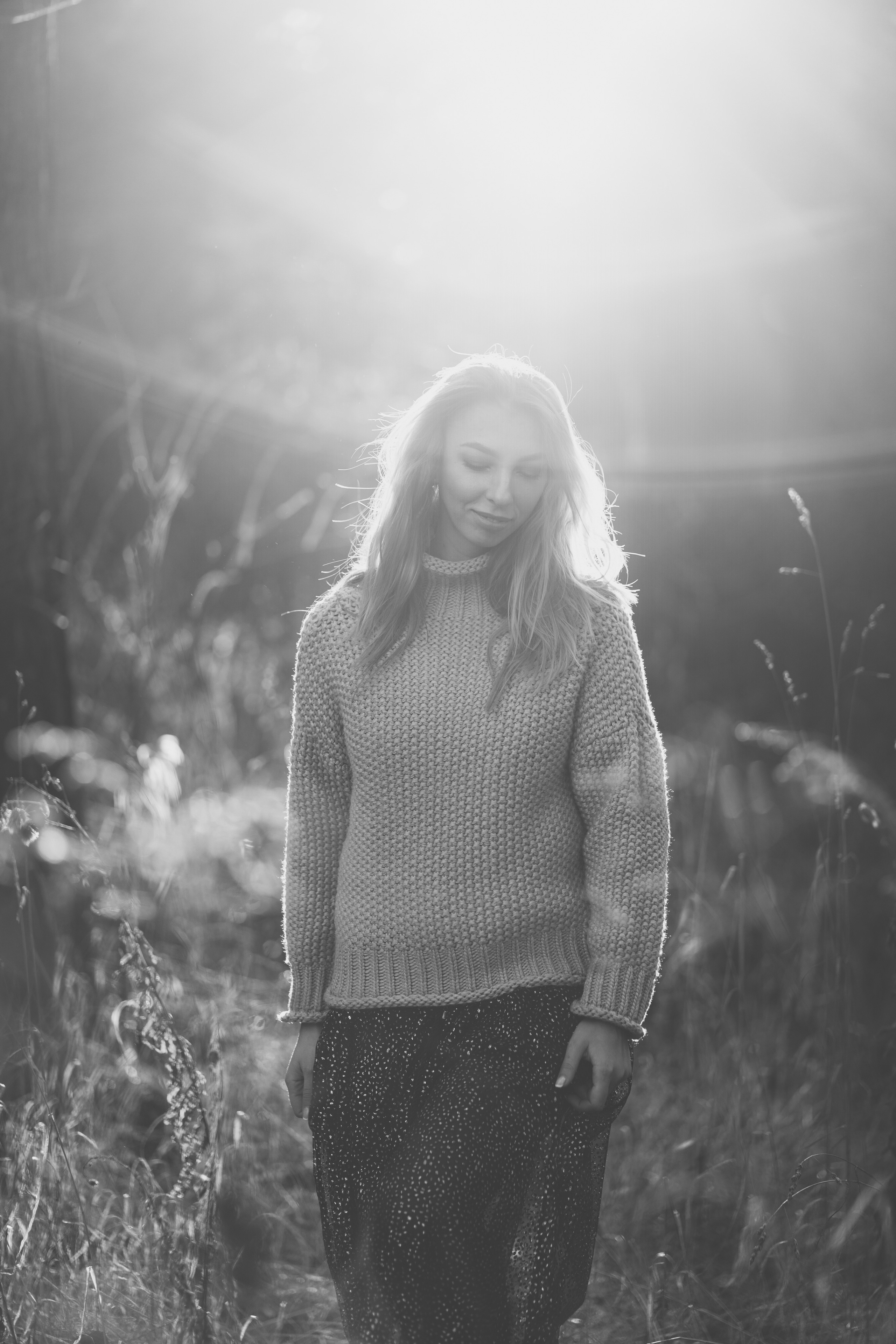 Девушка в вязанном свитере с горлом и легком платье, улыбается и идет через поле